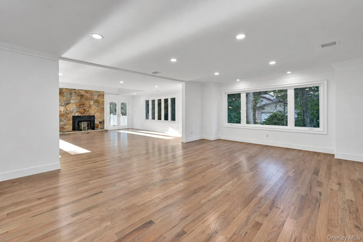 Hardwood flooring throughout, recessed lighting, stone-clad fireplace with black firebox, white double doors, and expansive windows Hardwood flooring throughout, recessed lighting, stone-clad fireplace with black firebox, white double doors, and expansive windows