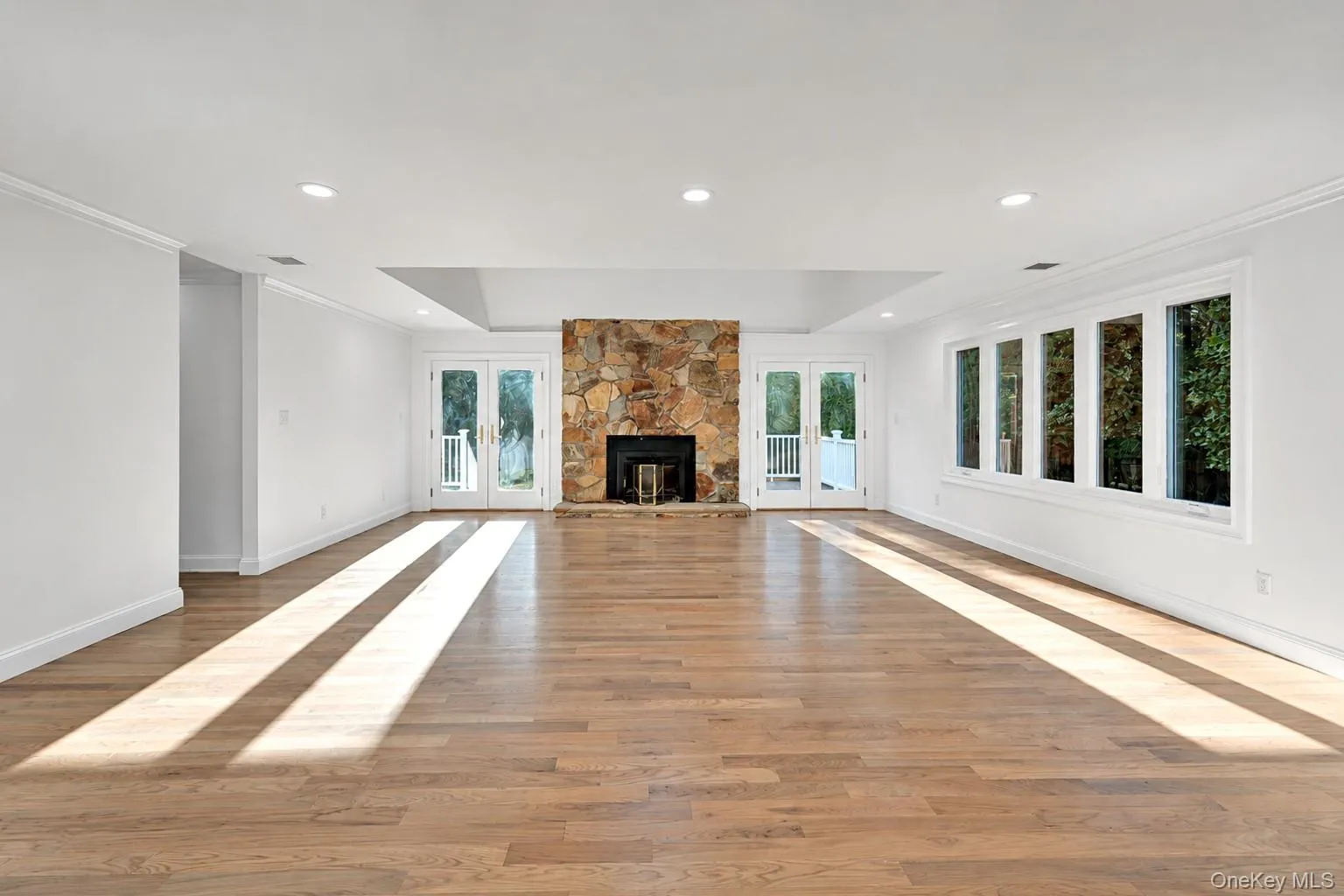 Spacious room featuring wood-finish flooring, a stone fireplace, and recessed lighting Spacious room featuring wood-finish flooring, a stone fireplace, and recessed lighting