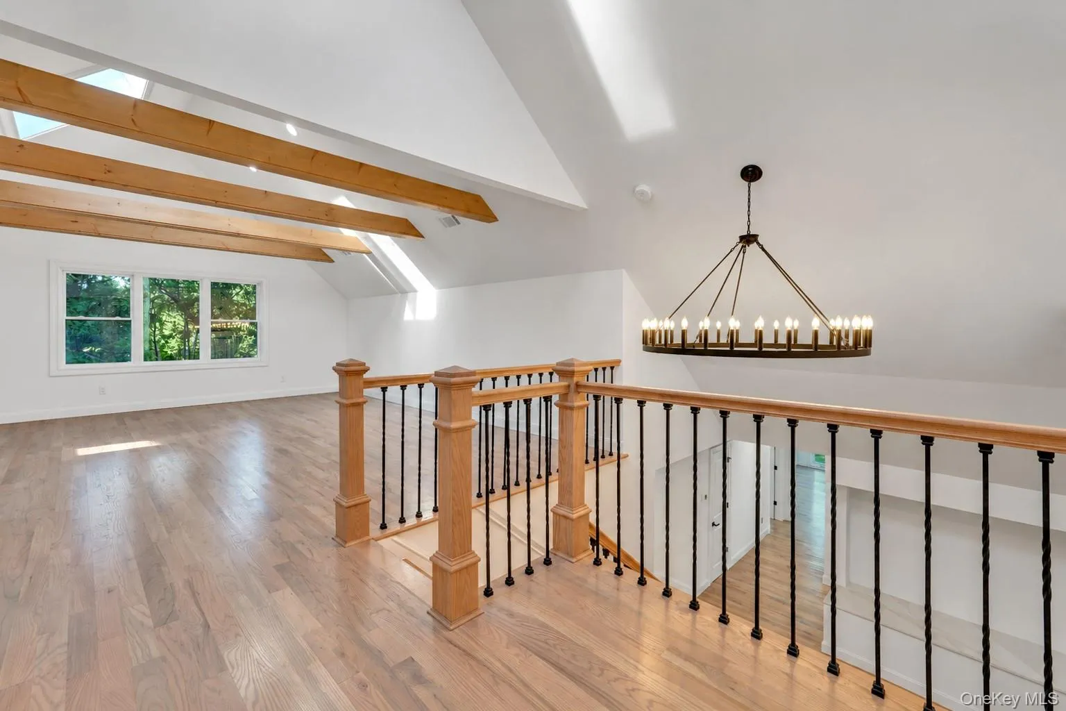 Vaulted ceiling with exposed wood beams and skylights, wood-finish flooring, wrought iron and wood balustrade, and an overhead chandelier Vaulted ceiling with exposed wood beams and skylights, wood-finish flooring, wrought iron and wood balustrade, and an overhead chandelier