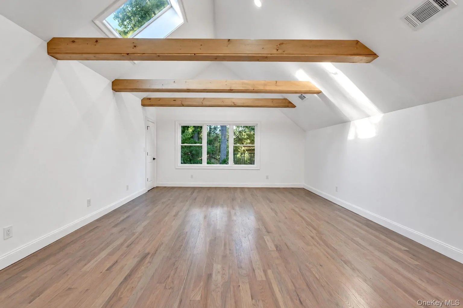 Vaulted ceiling with exposed wood beams, skylight, wood-finish flooring, and white trim Vaulted ceiling with exposed wood beams, skylight, wood-finish flooring, and white trim