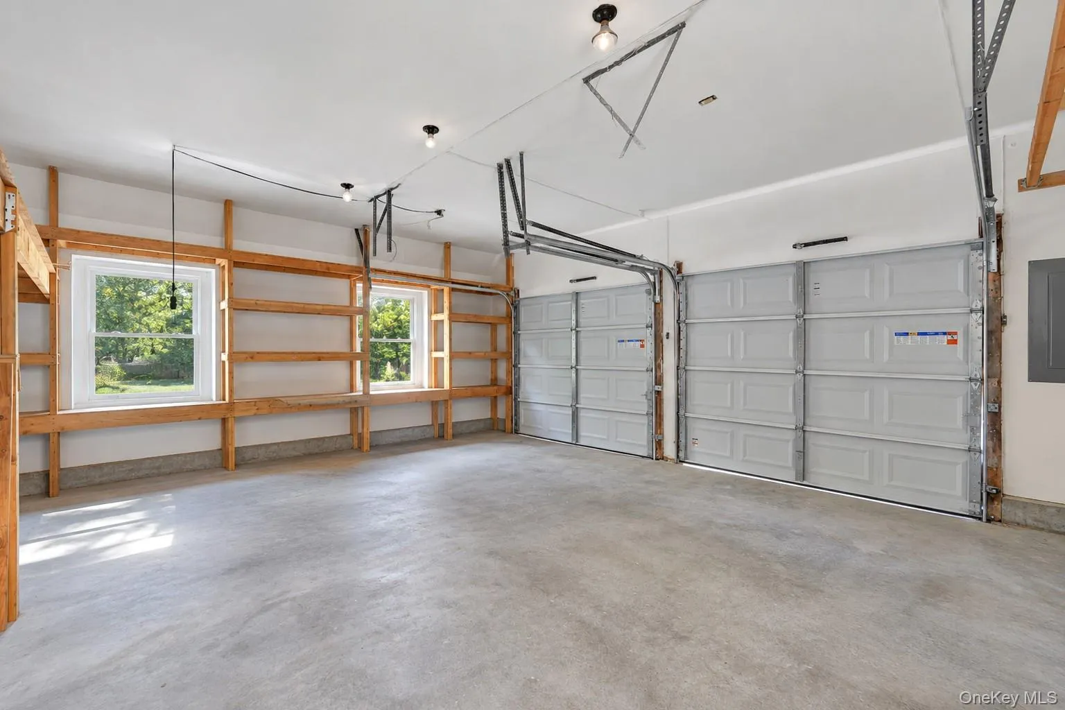Concrete flooring, two panel garage doors, two windows, built-in wooden shelving, and overhead lighting fixtures Concrete flooring, two panel garage doors, two windows, built-in wooden shelving, and overhead lighting fixtures