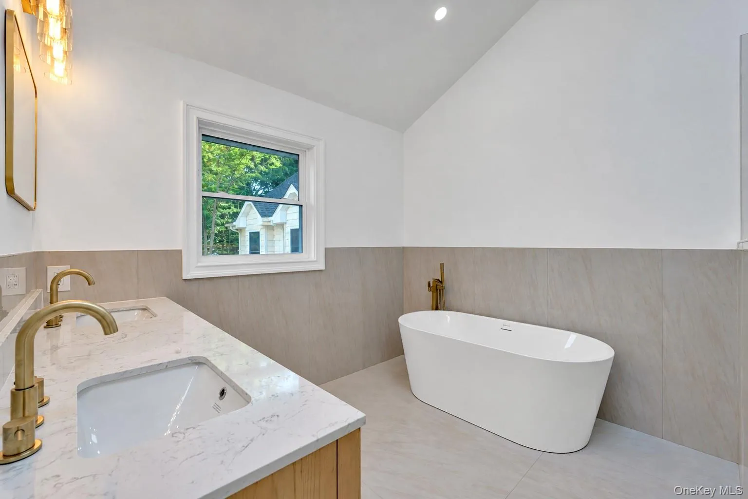 Freestanding soaking tub, dual vanity with undermount sinks, quartz countertop, gold-finish fixtures, and tiled walls Freestanding soaking tub, dual vanity with undermount sinks, quartz countertop, gold-finish fixtures, and tiled walls
