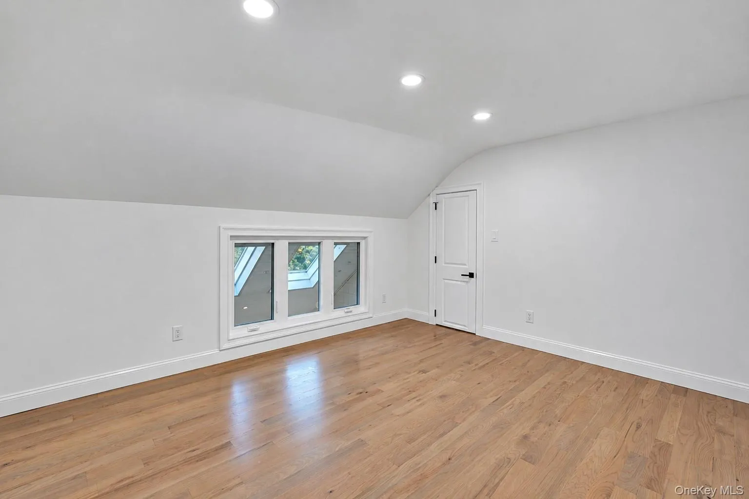 Wood-finish flooring, recessed lighting, attic-style ceilings, white interior door, and a multi-pane window Wood-finish flooring, recessed lighting, attic-style ceilings, white interior door, and a multi-pane window