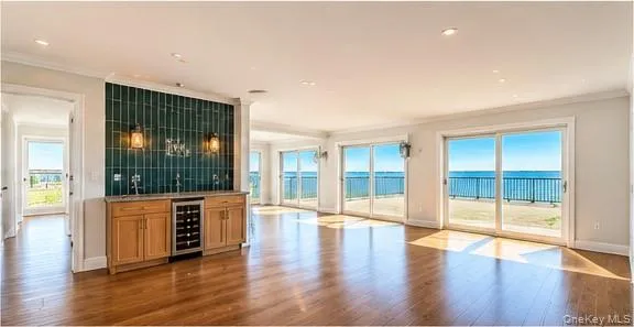 Hardwood flooring throughout, wet bar with wood cabinetry and dark green vertical tile, stainless steel beverage refrigerator, multiple sliding glass doors, and recessed lighting Hardwood flooring throughout, wet bar with wood cabinetry and dark green vertical tile, stainless steel beverage refrigerator, multiple sliding glass doors, and recessed lighting