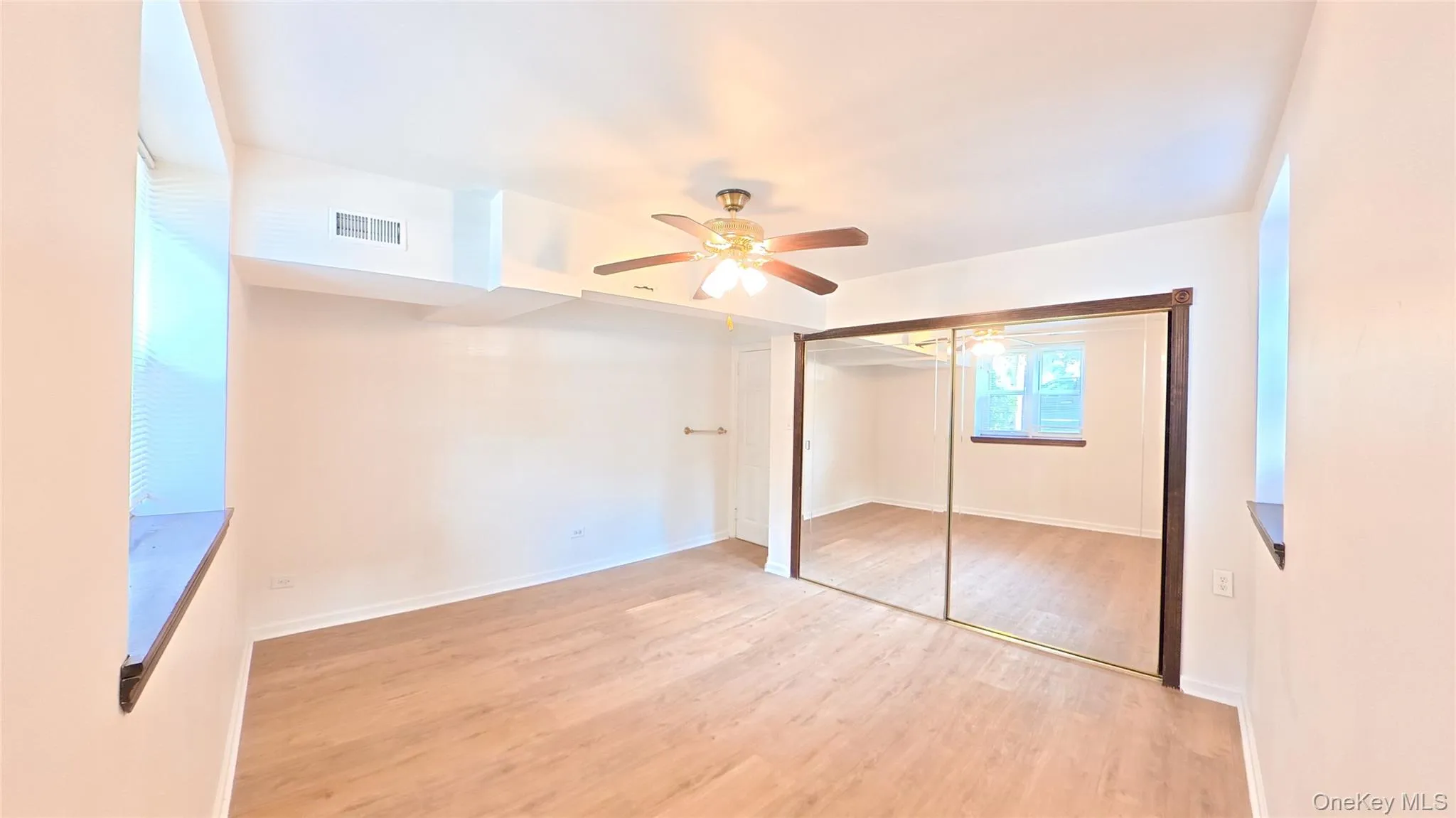 Light wood-finish flooring with a ceiling fan light fixture and multiple windows Light wood-finish flooring with a ceiling fan light fixture and multiple windows