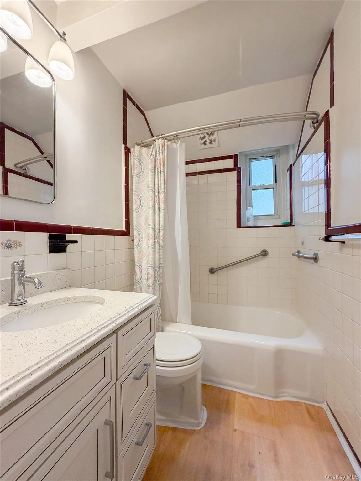 Bathroom featuring a single vanity with light countertop, wood-finish flooring, a full bathtub with grab bars Bathroom featuring a single vanity with light countertop, wood-finish flooring, a full bathtub with grab bars