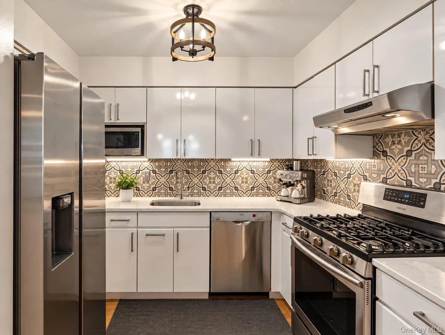 Contemporary kitchen featuring stainless steel appliances, white cabinetry, patterned tile backsplash, and light countertops Contemporary kitchen featuring stainless steel appliances, white cabinetry, patterned tile backsplash, and light countertops