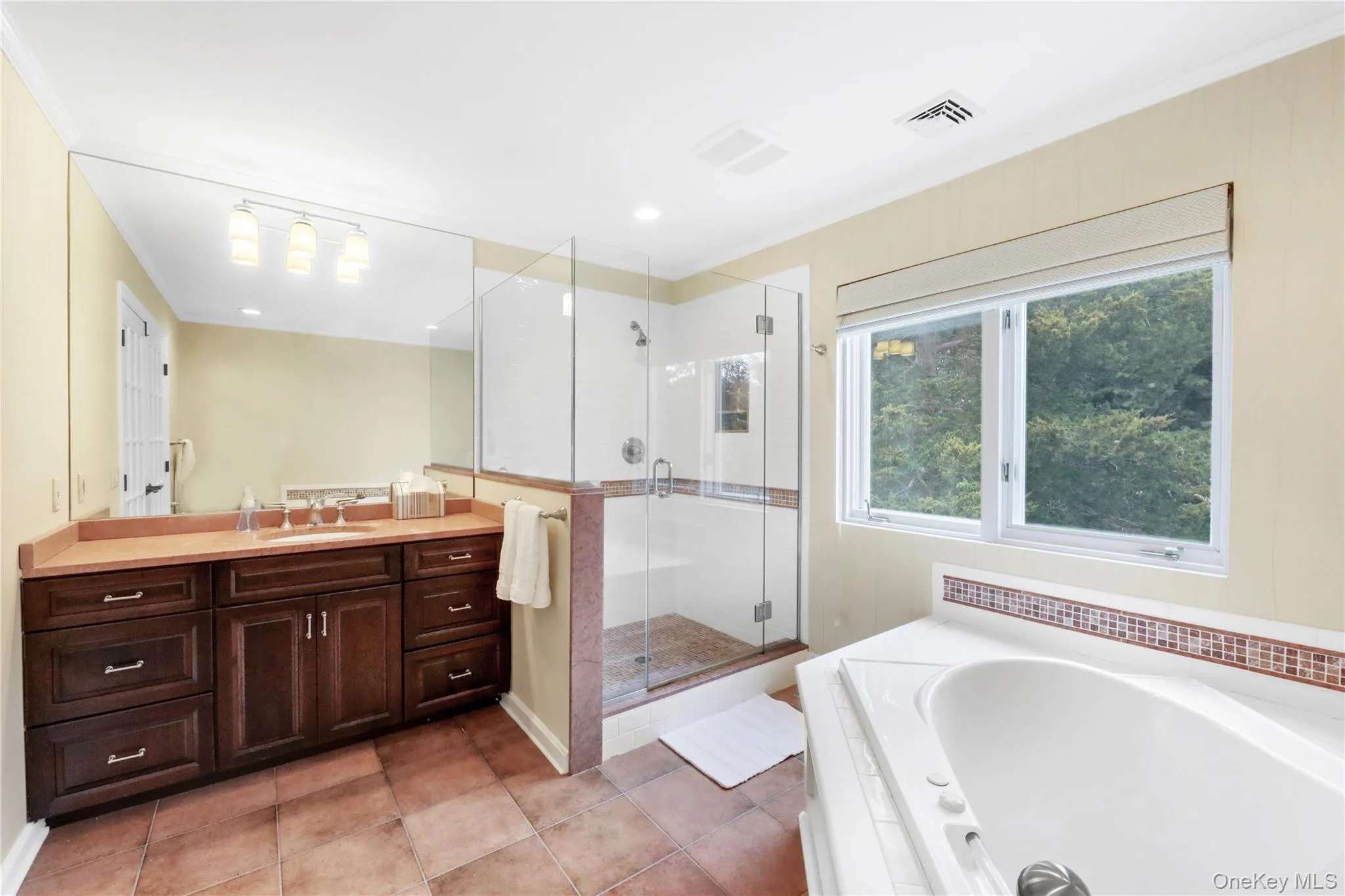 Full bath featuring vanity, a garden tub, a stall shower, light tile patterned flooring, and crown molding Full bath featuring vanity, a garden tub, a stall shower, light tile patterned flooring, and crown molding