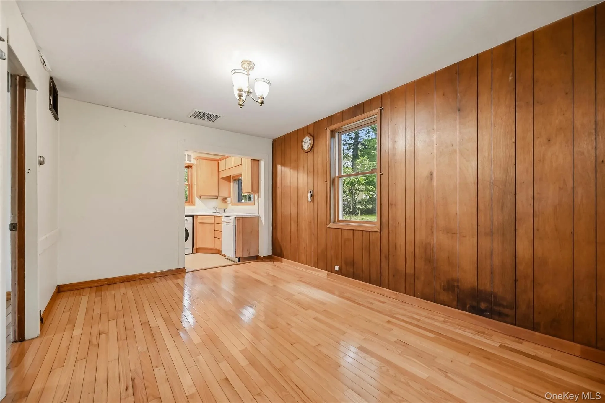 Hardwood flooring throughout, a single window, a ceiling-mounted light fixture, and wood-paneled wall Hardwood flooring throughout, a single window, a ceiling-mounted light fixture, and wood-paneled wall