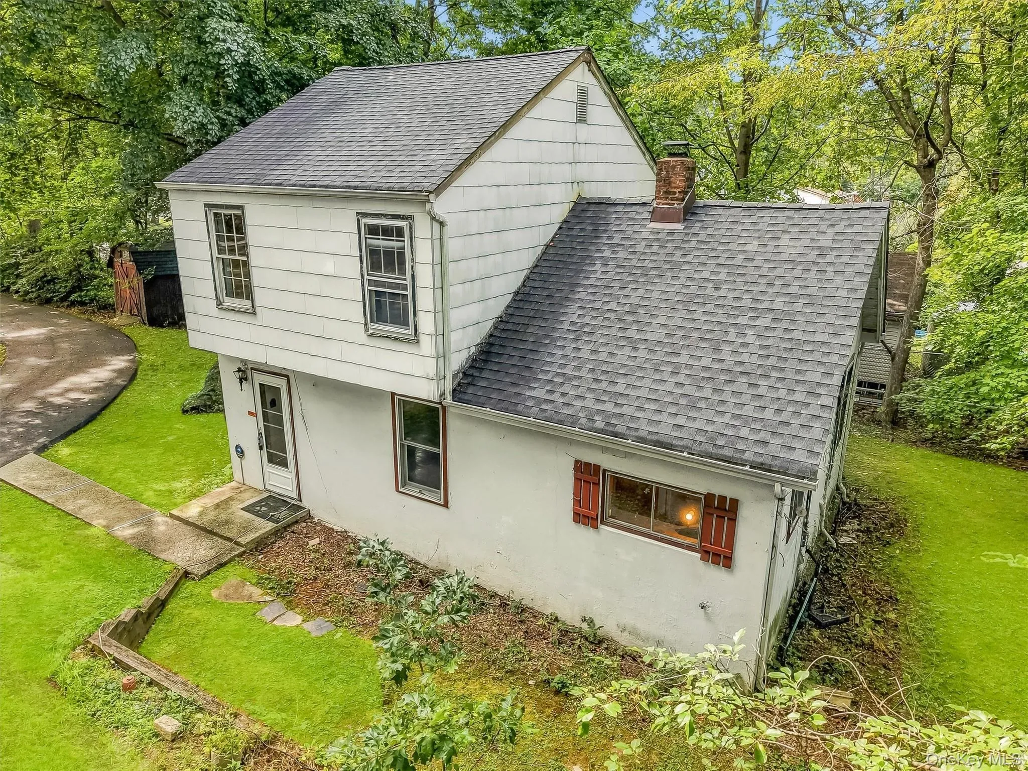 White siding exterior with a dark shingle roof, chimney, and red window shutters White siding exterior with a dark shingle roof, chimney, and red window shutters