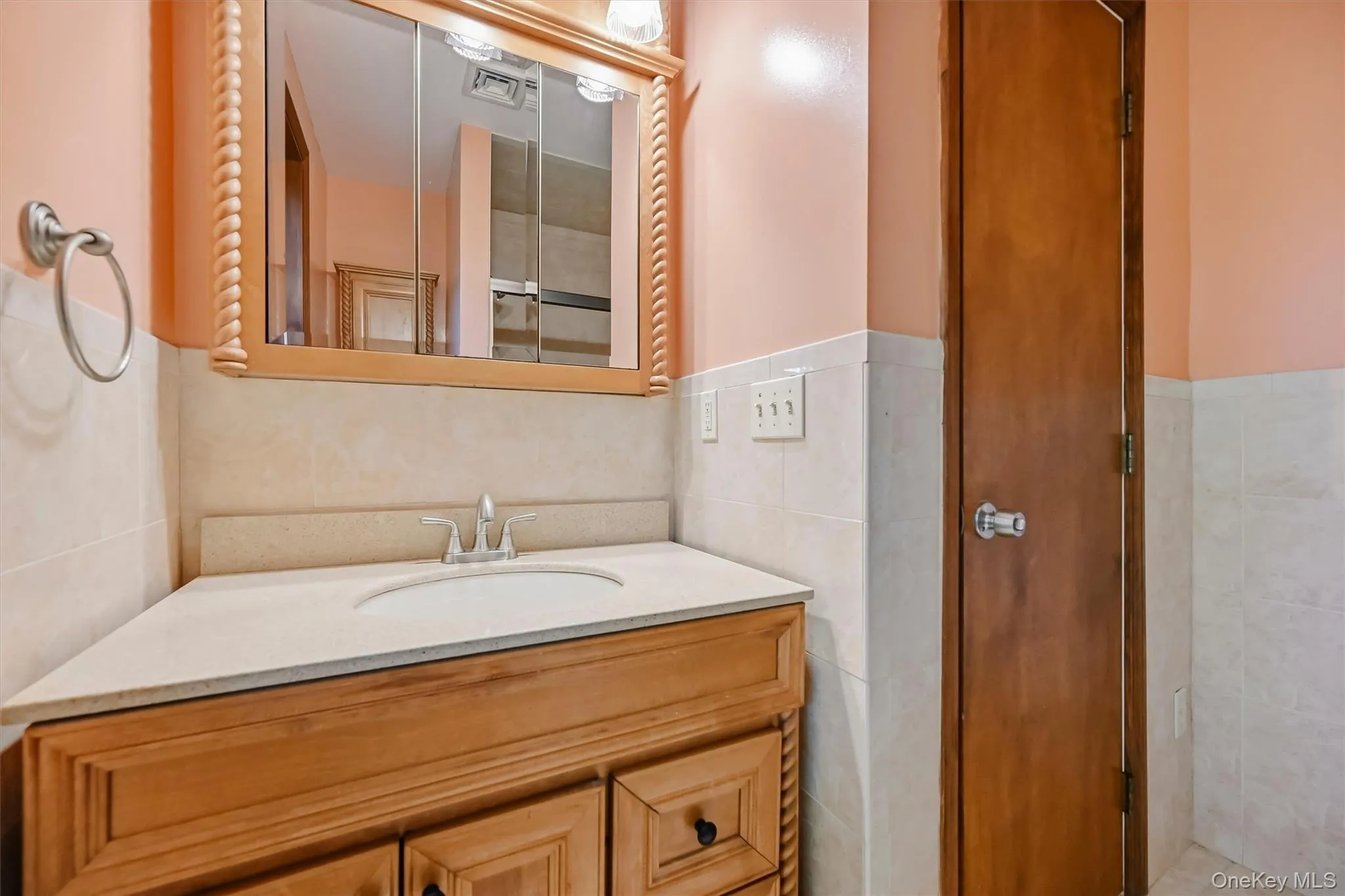 Corner vanity with integrated sink, wood-finish cabinetry, light-toned countertop, and recessed medicine cabinet with overhead lighting Corner vanity with integrated sink, wood-finish cabinetry, light-toned countertop, and recessed medicine cabinet with overhead lighting