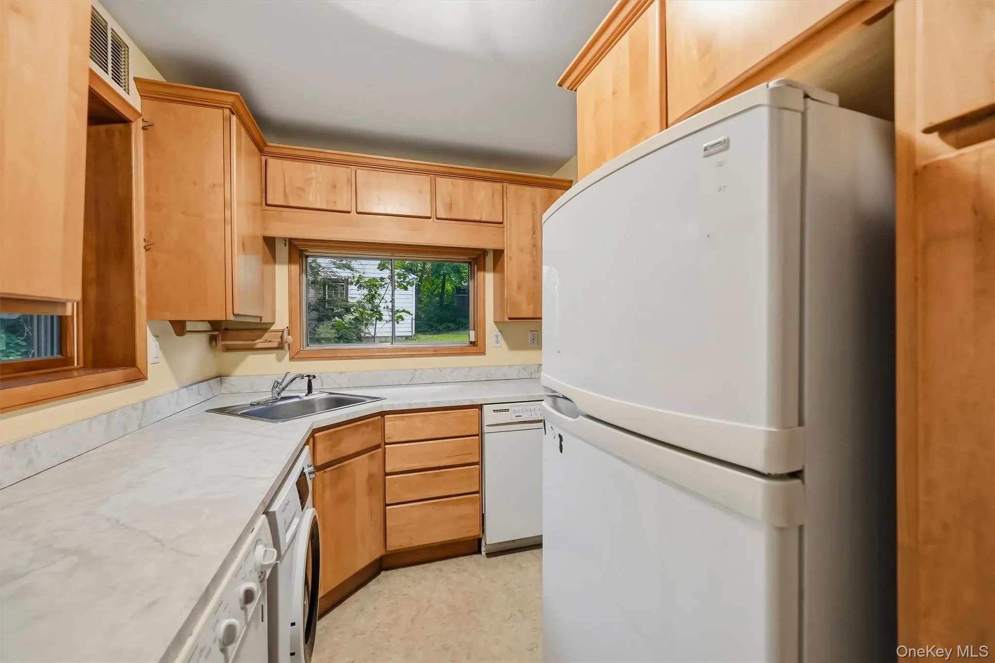 L-shaped kitchen featuring wood-finish cabinetry, light-toned countertops, and sink L-shaped kitchen featuring wood-finish cabinetry, light-toned countertops, and sink