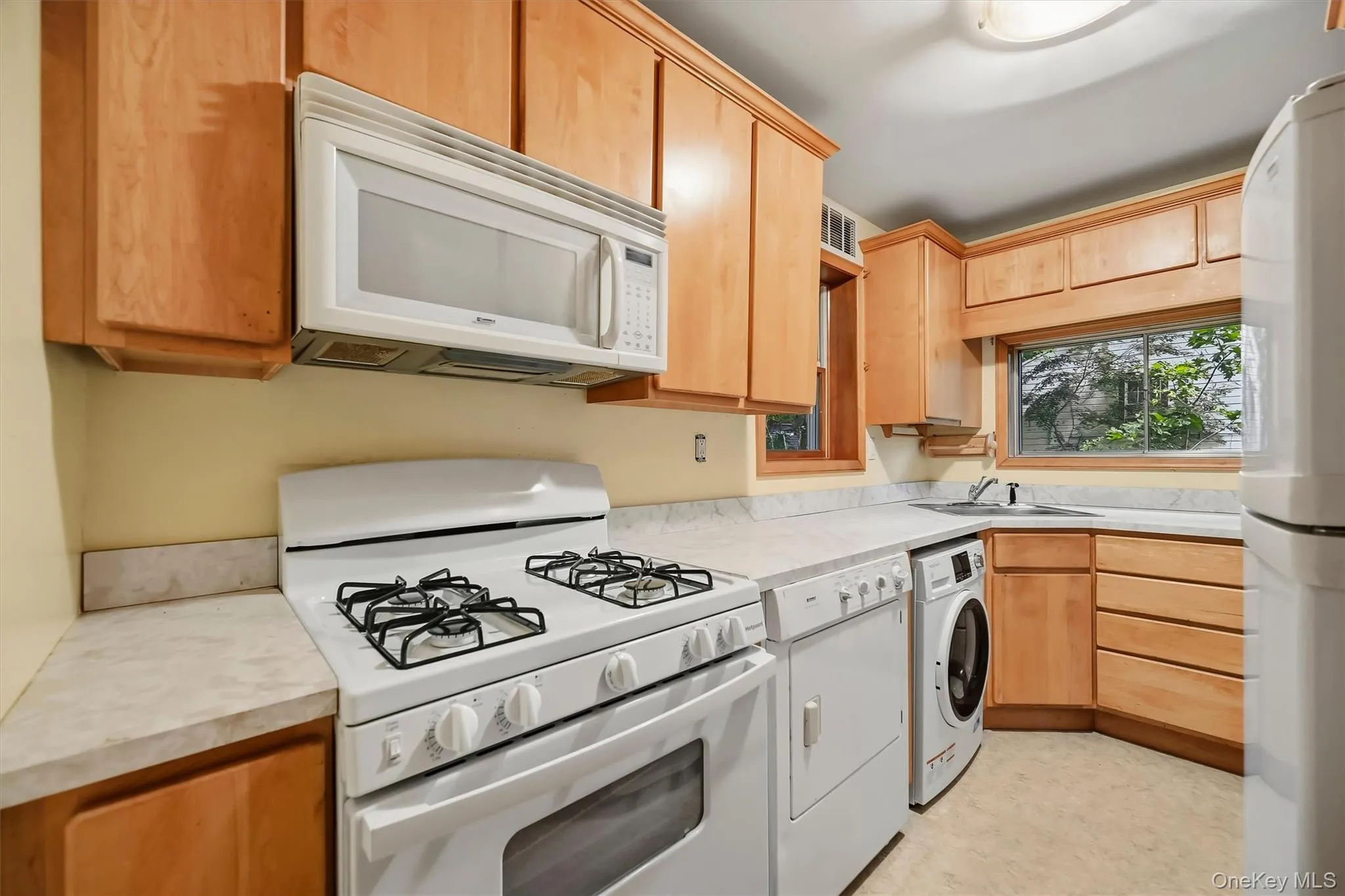 Kitchen featuring light wood-finish cabinetry, white appliances, and a built-in washing machine Kitchen featuring light wood-finish cabinetry, white appliances, and a built-in washing machine