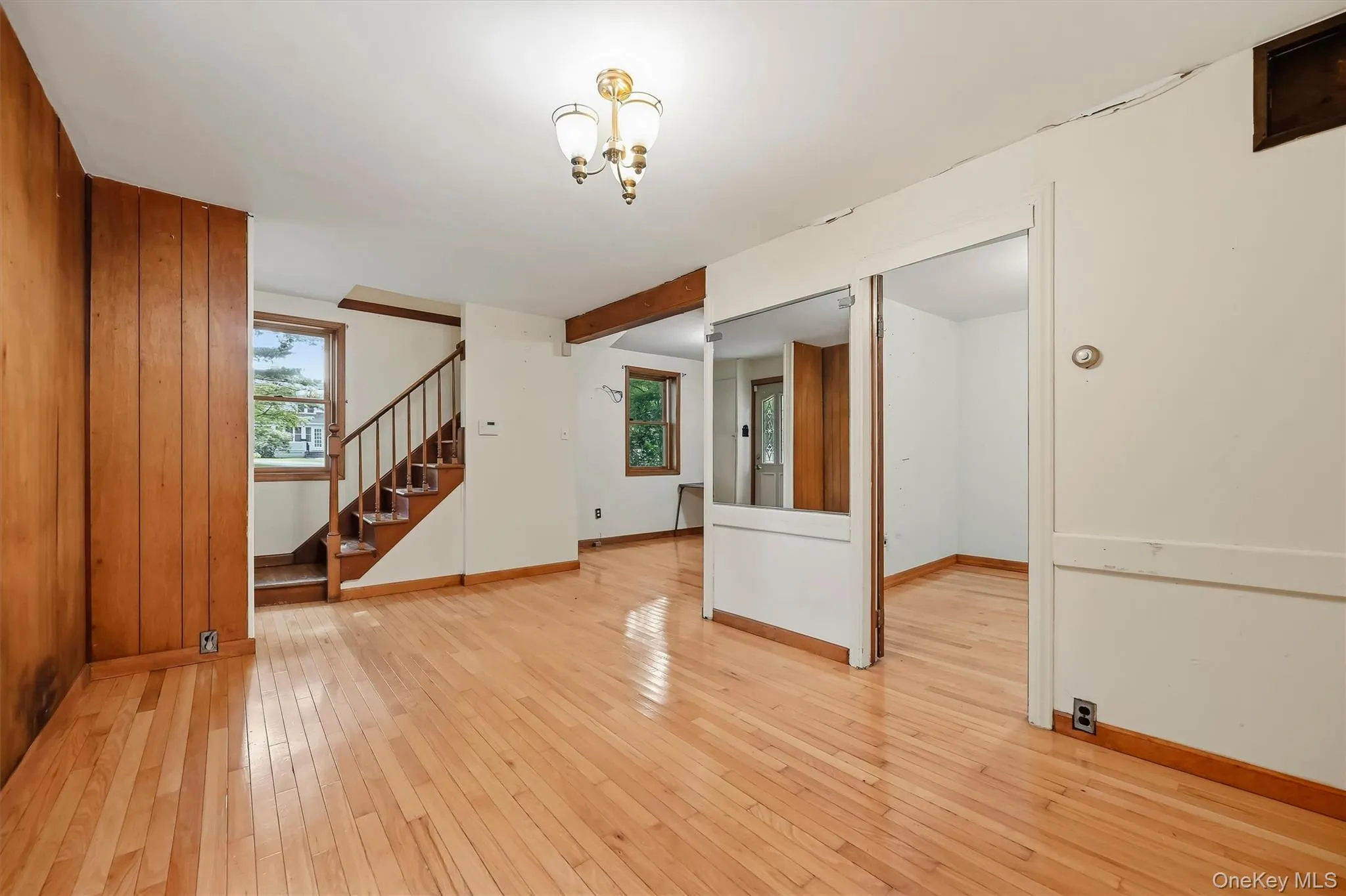 Hardwood flooring, wood paneling, wood staircase with dark railings, multiple windows, and a ceiling-mounted light fixture Hardwood flooring, wood paneling, wood staircase with dark railings, multiple windows, and a ceiling-mounted light fixture