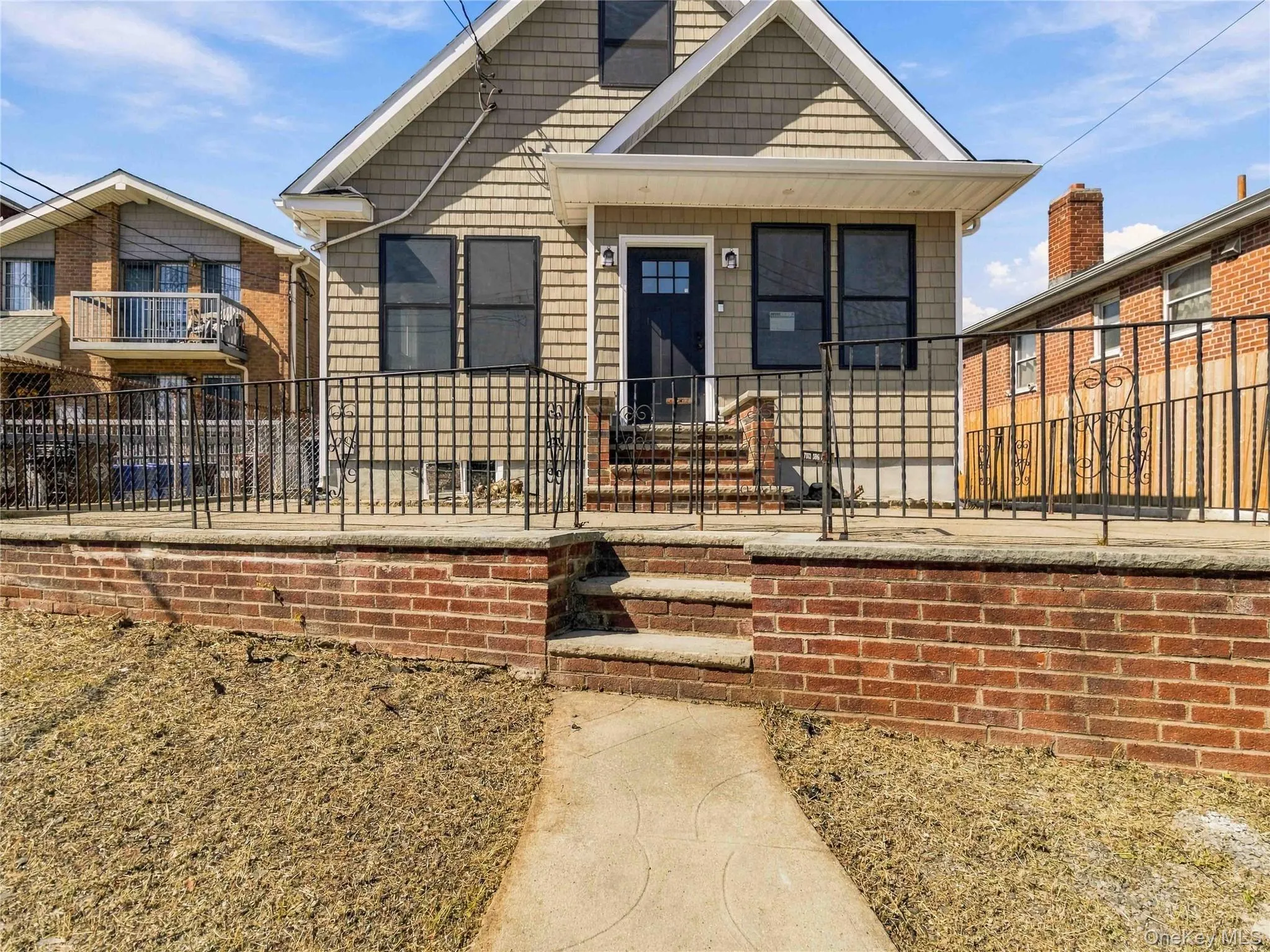 Shingle siding exterior with black window frames, a dark entry door, a brick foundation, and wrought iron fencing Shingle siding exterior with black window frames, a dark entry door, a brick foundation, and wrought iron fencing