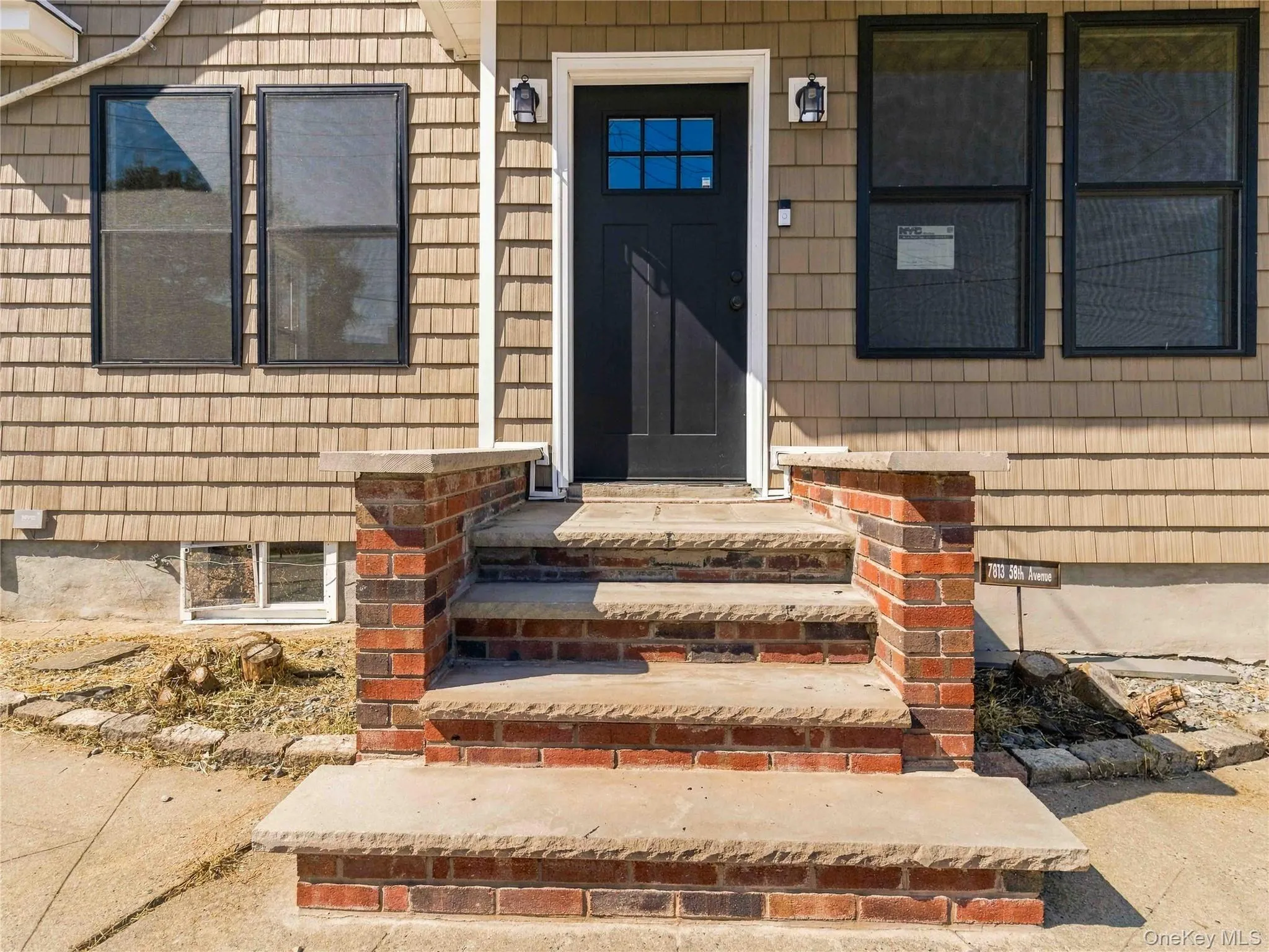 Shingle siding exterior with a dark-paneled entry door, brick and stone steps, and exterior wall sconces Shingle siding exterior with a dark-paneled entry door, brick and stone steps, and exterior wall sconces