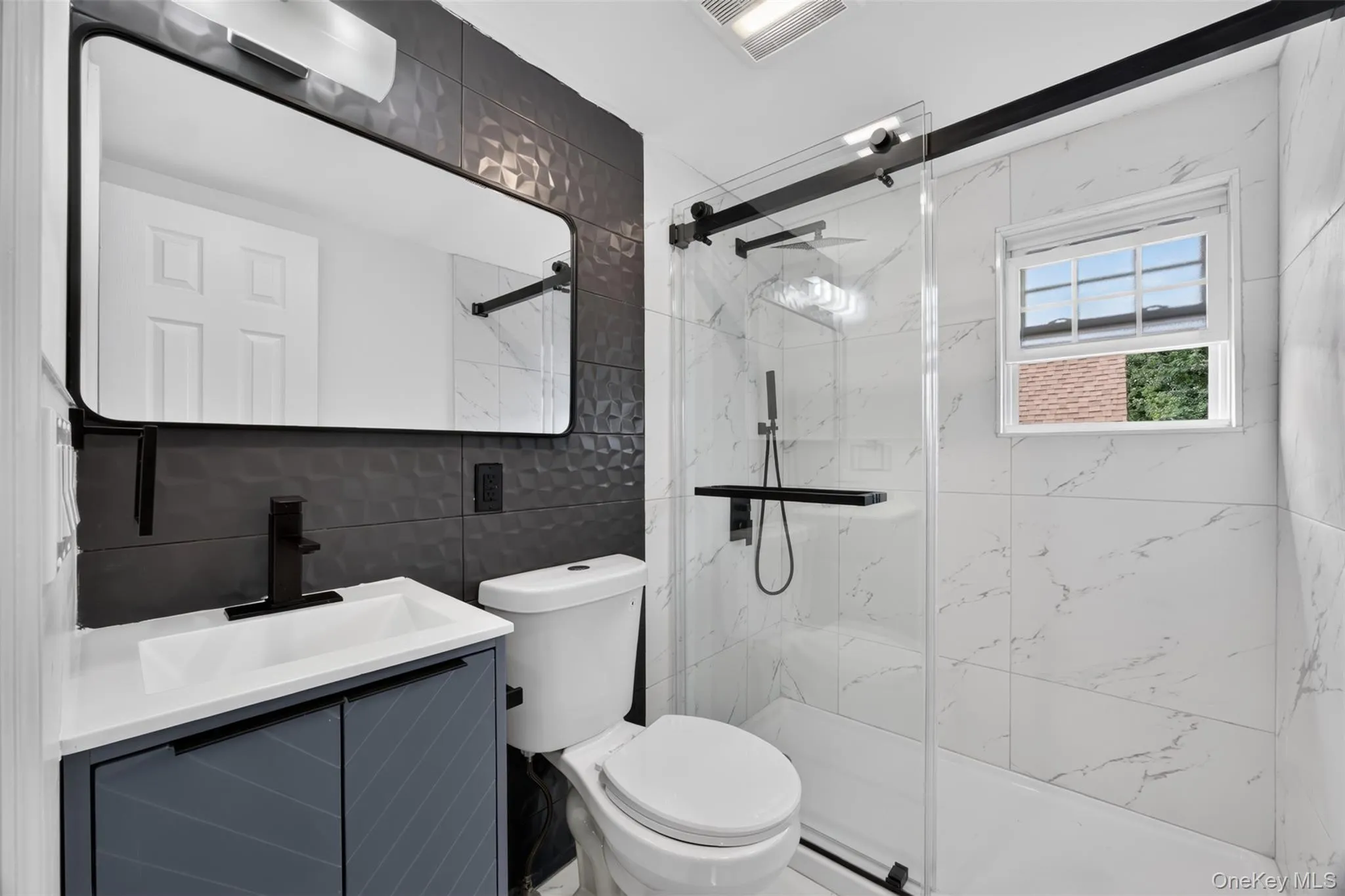 Bathroom featuring a textured accent wall, a floating vanity with a vessel sink, a matte black faucet, a large rectangular mirror, and a glass-enclosed shower with subway tile surround Bathroom featuring a textured accent wall, a floating vanity with a vessel sink, a matte black faucet, a large rectangular mirror, and a glass-enclosed shower with subway tile surround