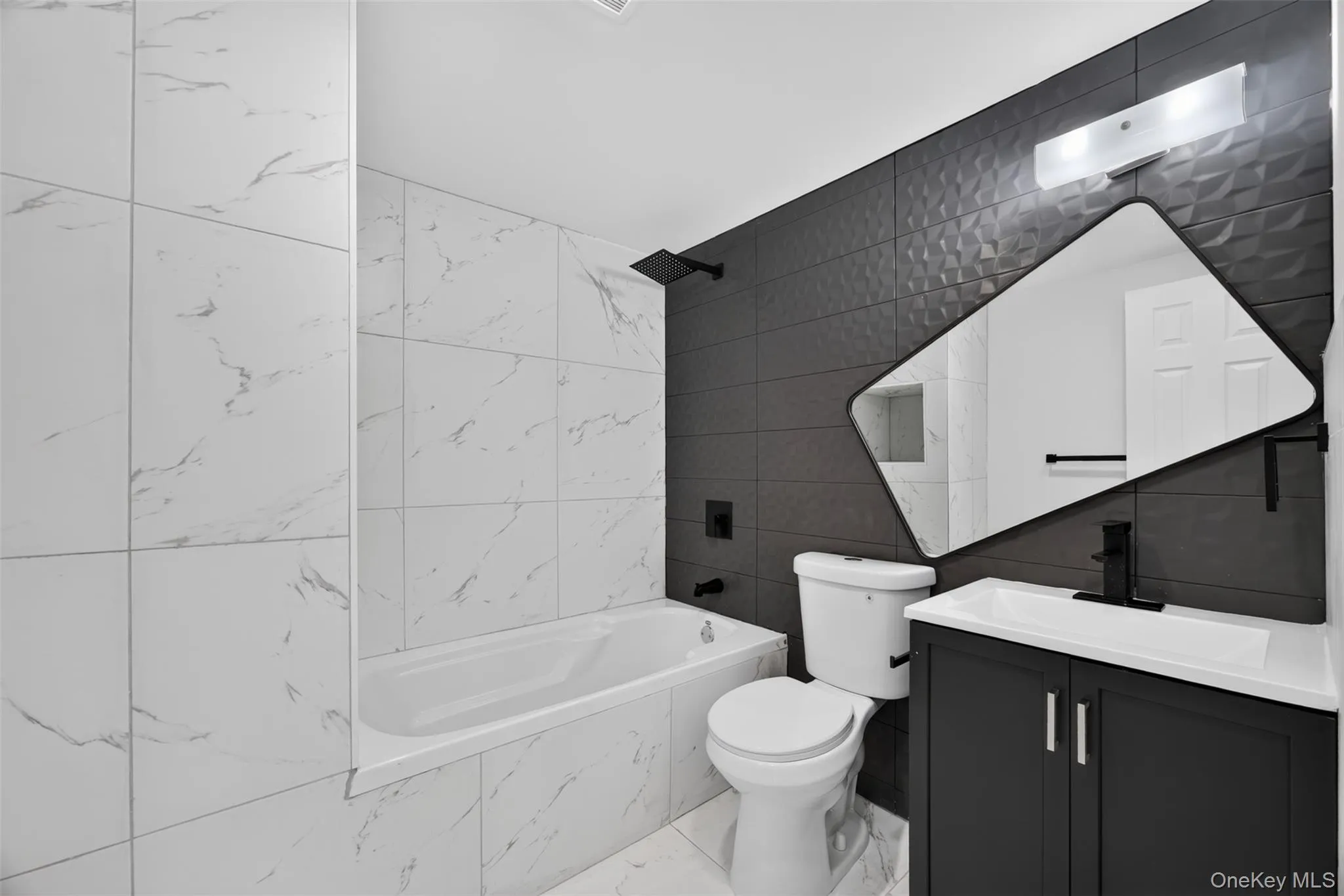 Floor-to-ceiling white marble-look tiling, dark textured accent wall, integrated bathtub with matte black fixtures, contemporary vanity with a contrasting white sink, and a uniquely shaped wall mirror Floor-to-ceiling white marble-look tiling, dark textured accent wall, integrated bathtub with matte black fixtures, contemporary vanity with a contrasting white sink, and a uniquely shaped wall mirror