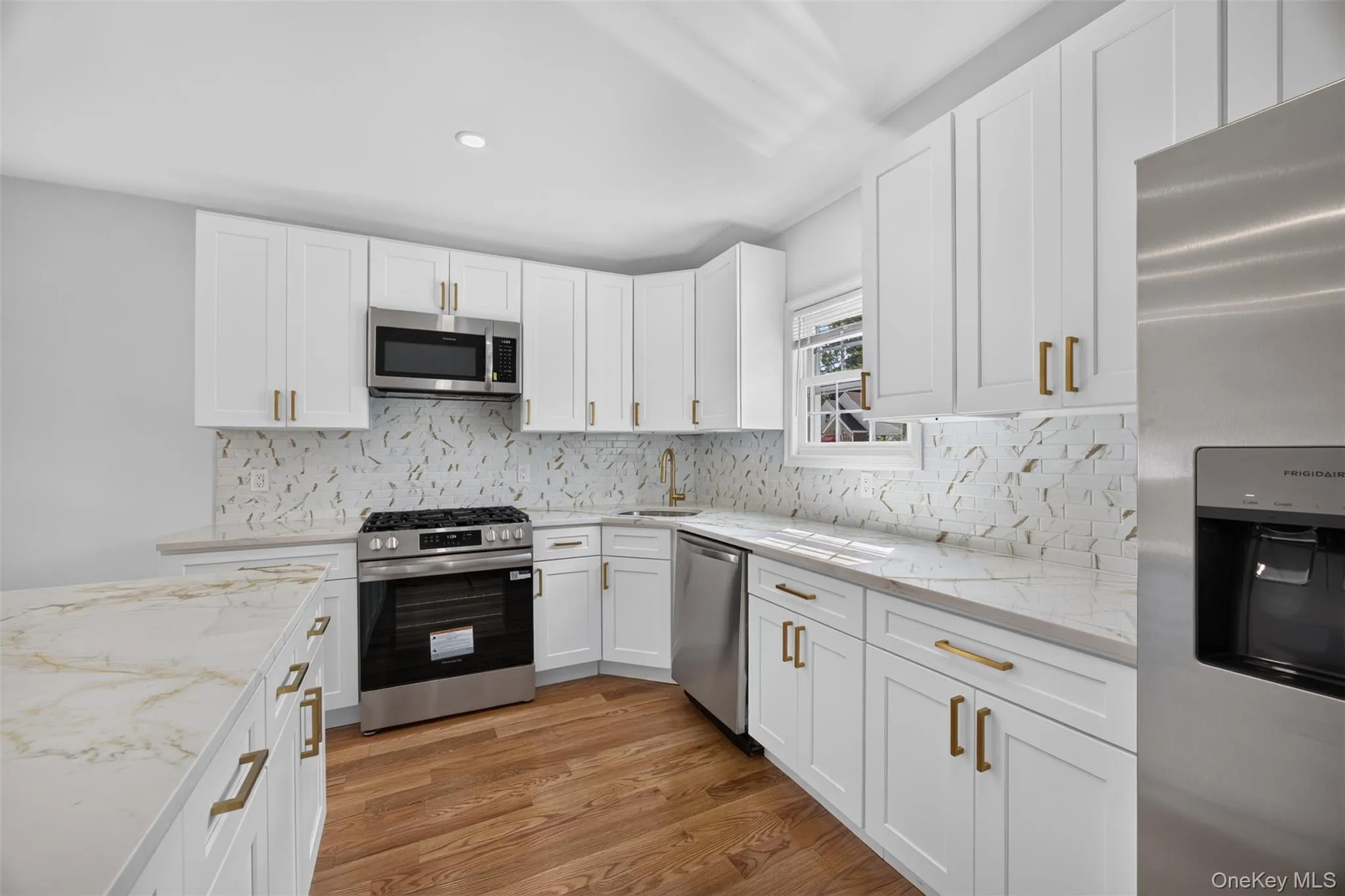Kitchen featuring white shaker cabinetry, stainless steel appliances, quartz countertops, a decorative tile backsplash, and wood-finish flooring Kitchen featuring white shaker cabinetry, stainless steel appliances, quartz countertops, a decorative tile backsplash, and wood-finish flooring