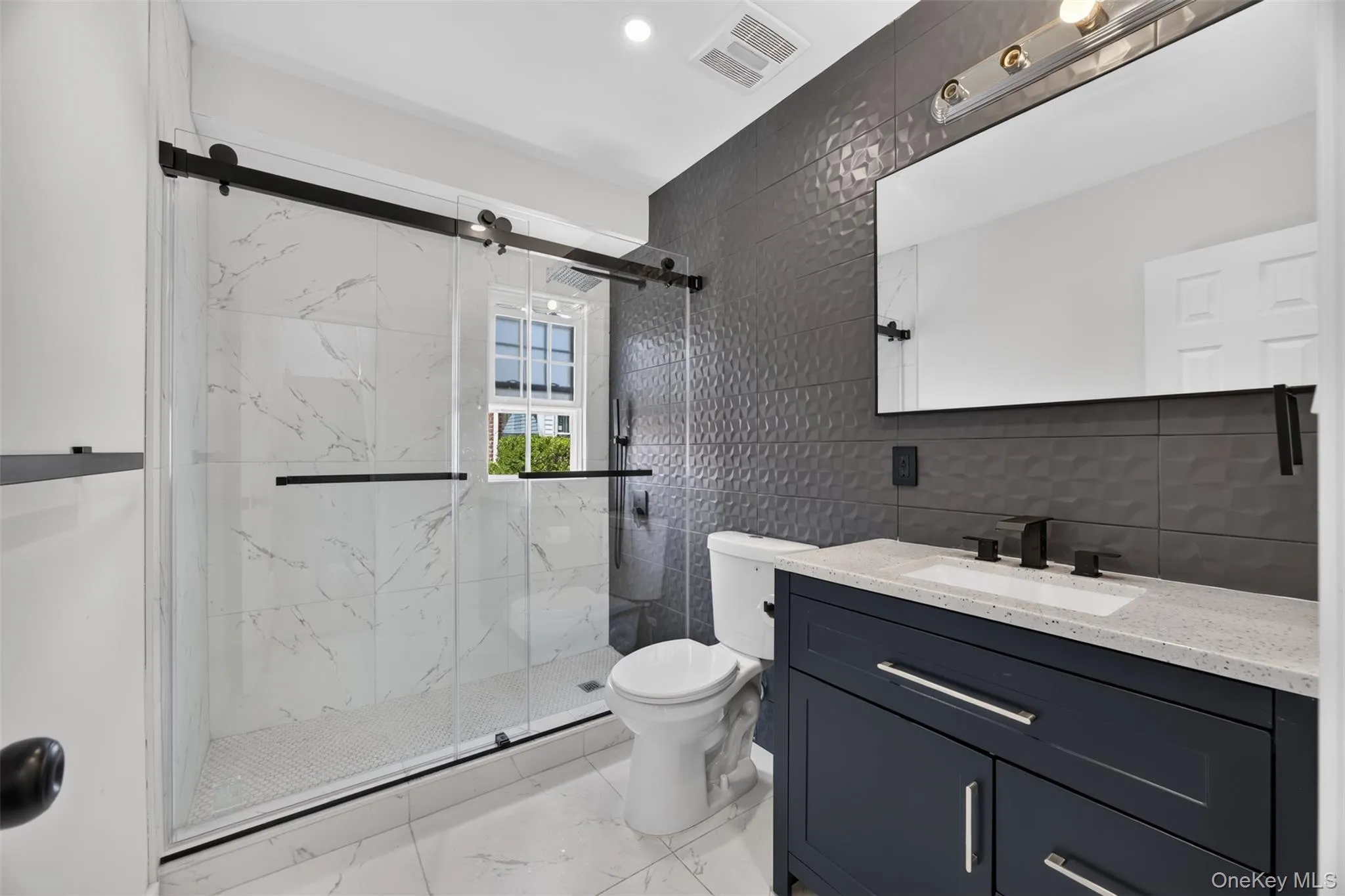 Barn door style shower enclosure with clear glass, marble-look shower wall tiles, and a mosaic tile shower floor Barn door style shower enclosure with clear glass, marble-look shower wall tiles, and a mosaic tile shower floor