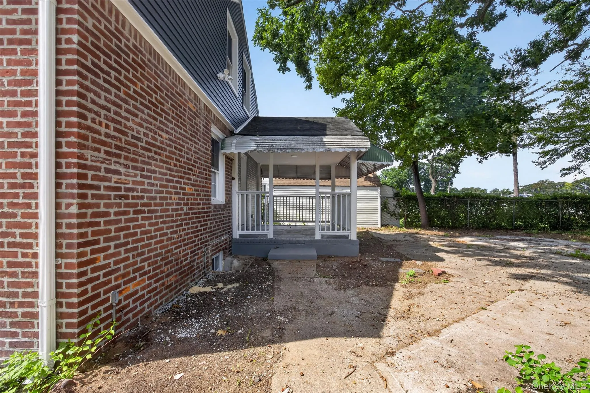 Brick exterior with a covered porch, white railing, and mature trees Brick exterior with a covered porch, white railing, and mature trees