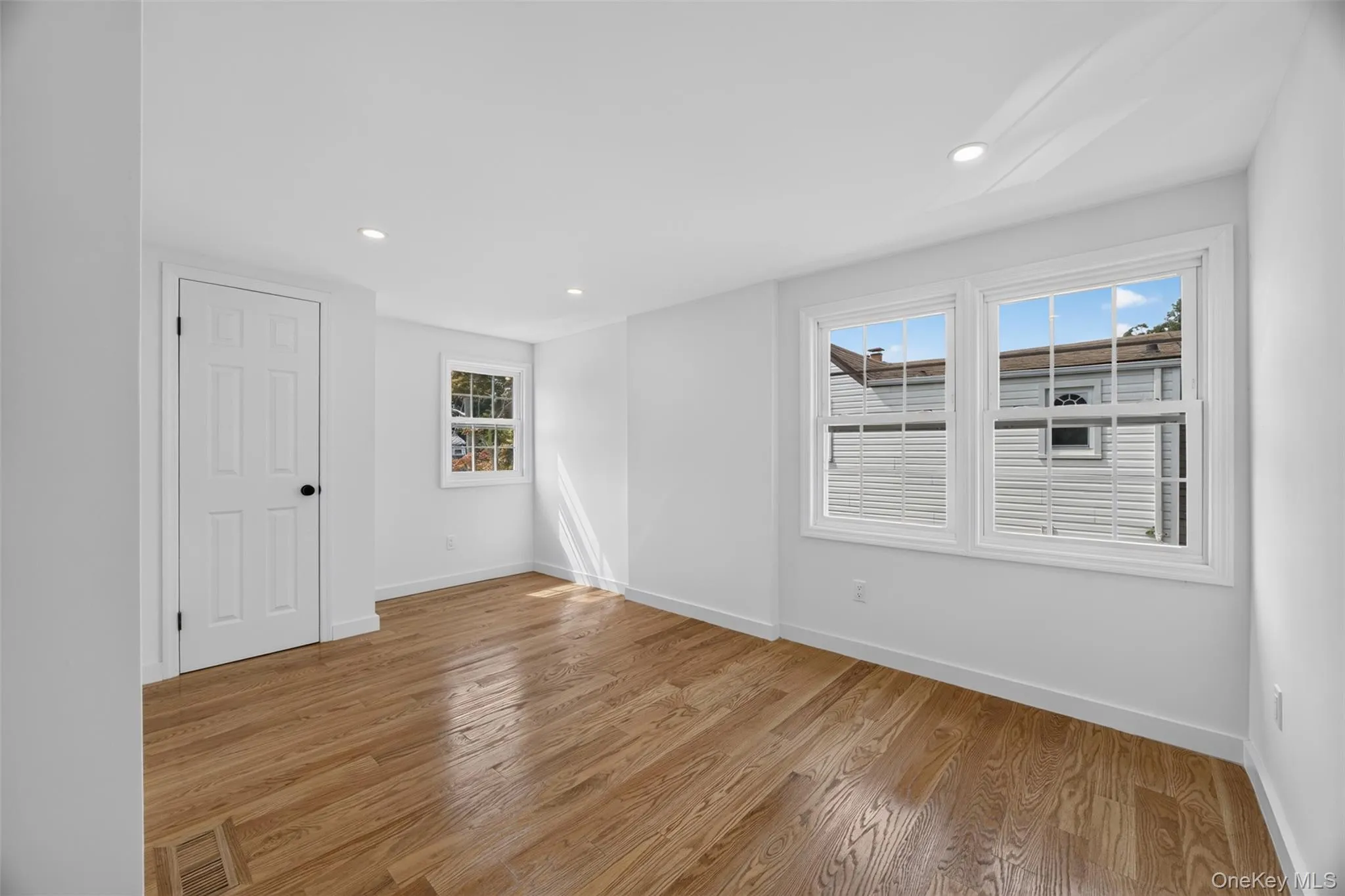 Hardwood flooring, recessed lighting, white trim, multiple windows, and a six-panel door Hardwood flooring, recessed lighting, white trim, multiple windows, and a six-panel door
