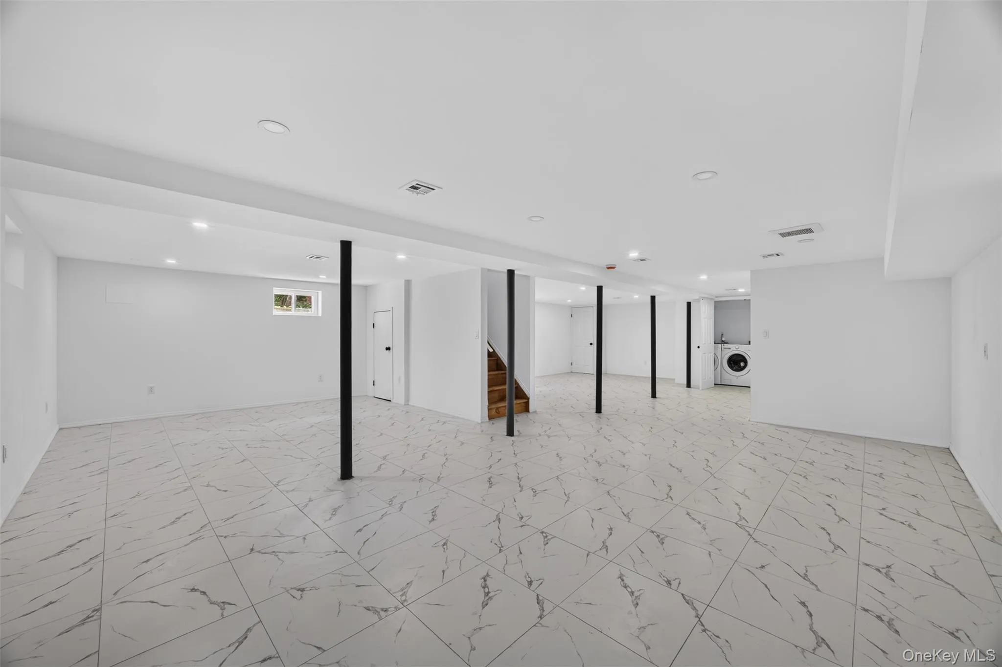 Expansive lower level with light-toned marble-look tile flooring, recessed lighting, a laundry area, and a wood staircase Expansive lower level with light-toned marble-look tile flooring, recessed lighting, a laundry area, and a wood staircase