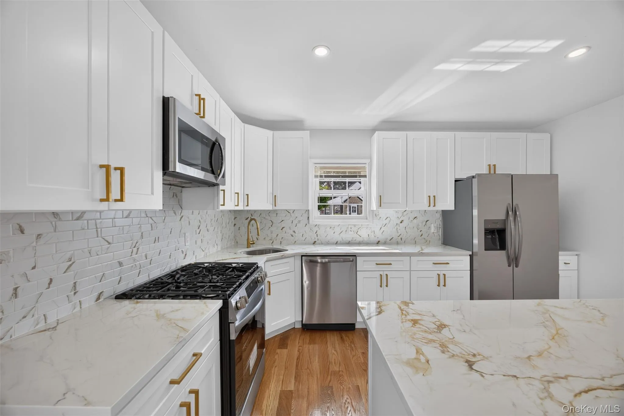 White shaker-style cabinetry with gold-tone hardware, stainless steel appliances, marble-look countertops, and wood-finish flooring White shaker-style cabinetry with gold-tone hardware, stainless steel appliances, marble-look countertops, and wood-finish flooring