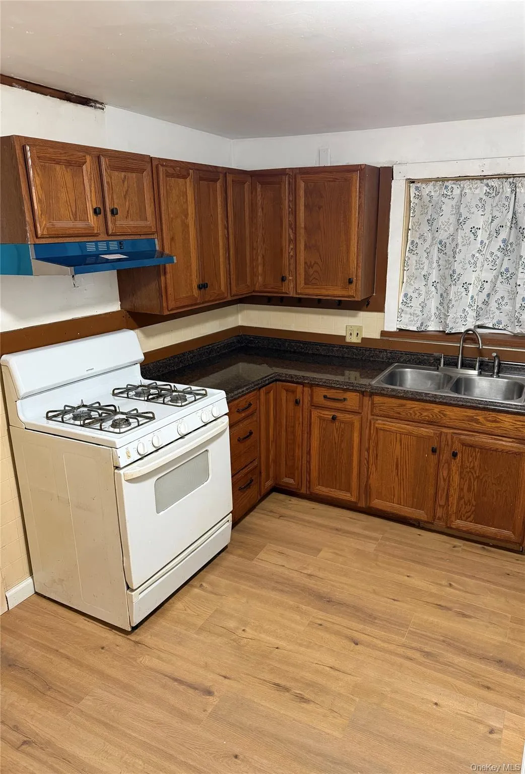 Kitchen with white gas range oven, dark countertops, brown cabinetry, and light wood finished floors Kitchen with white gas range oven, dark countertops, brown cabinetry, and light wood finished floors