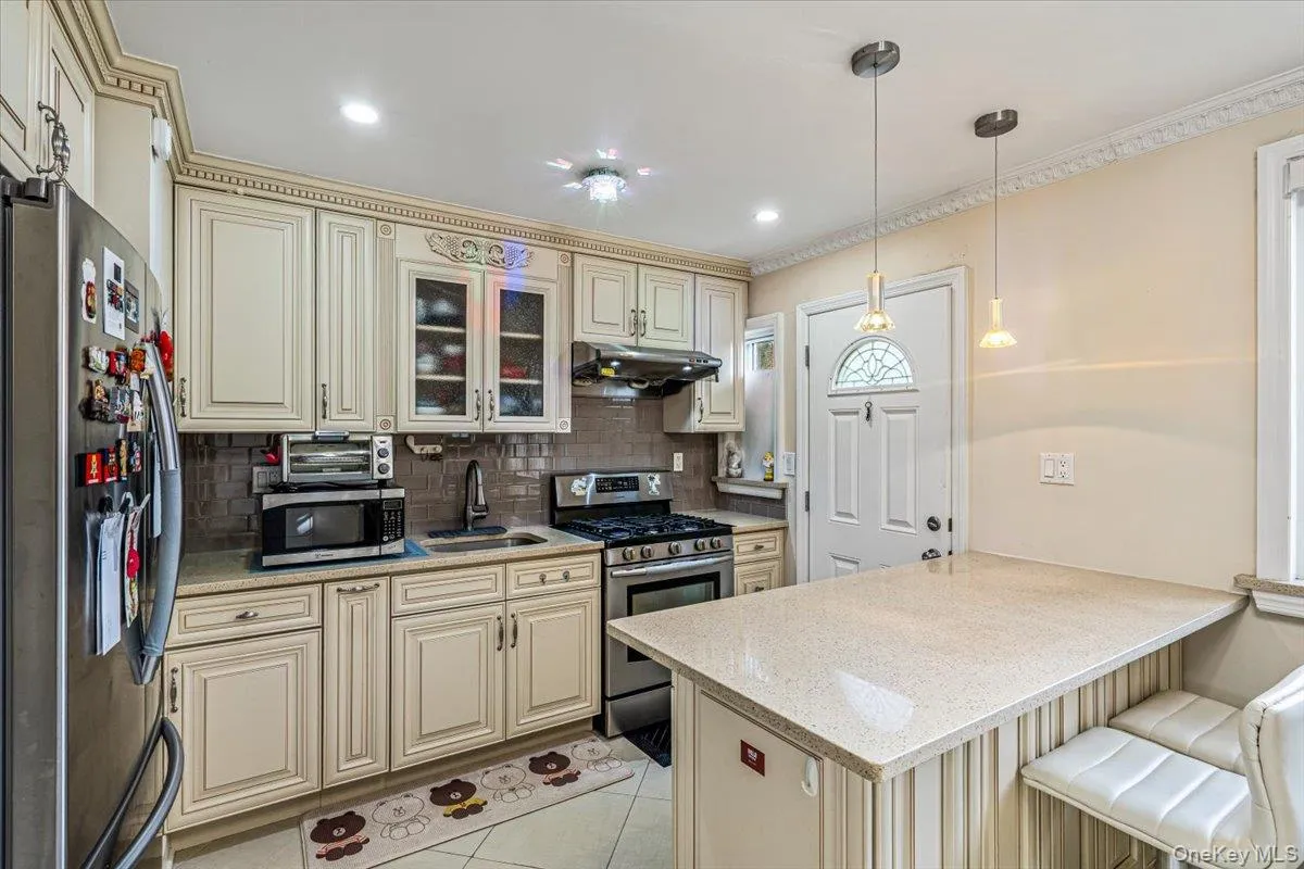 Kitchen featuring light-toned cabinetry, stainless steel appliances, a tile backsplash, and a breakfast bar with pendant lighting Kitchen featuring light-toned cabinetry, stainless steel appliances, a tile backsplash, and a breakfast bar with pendant lighting