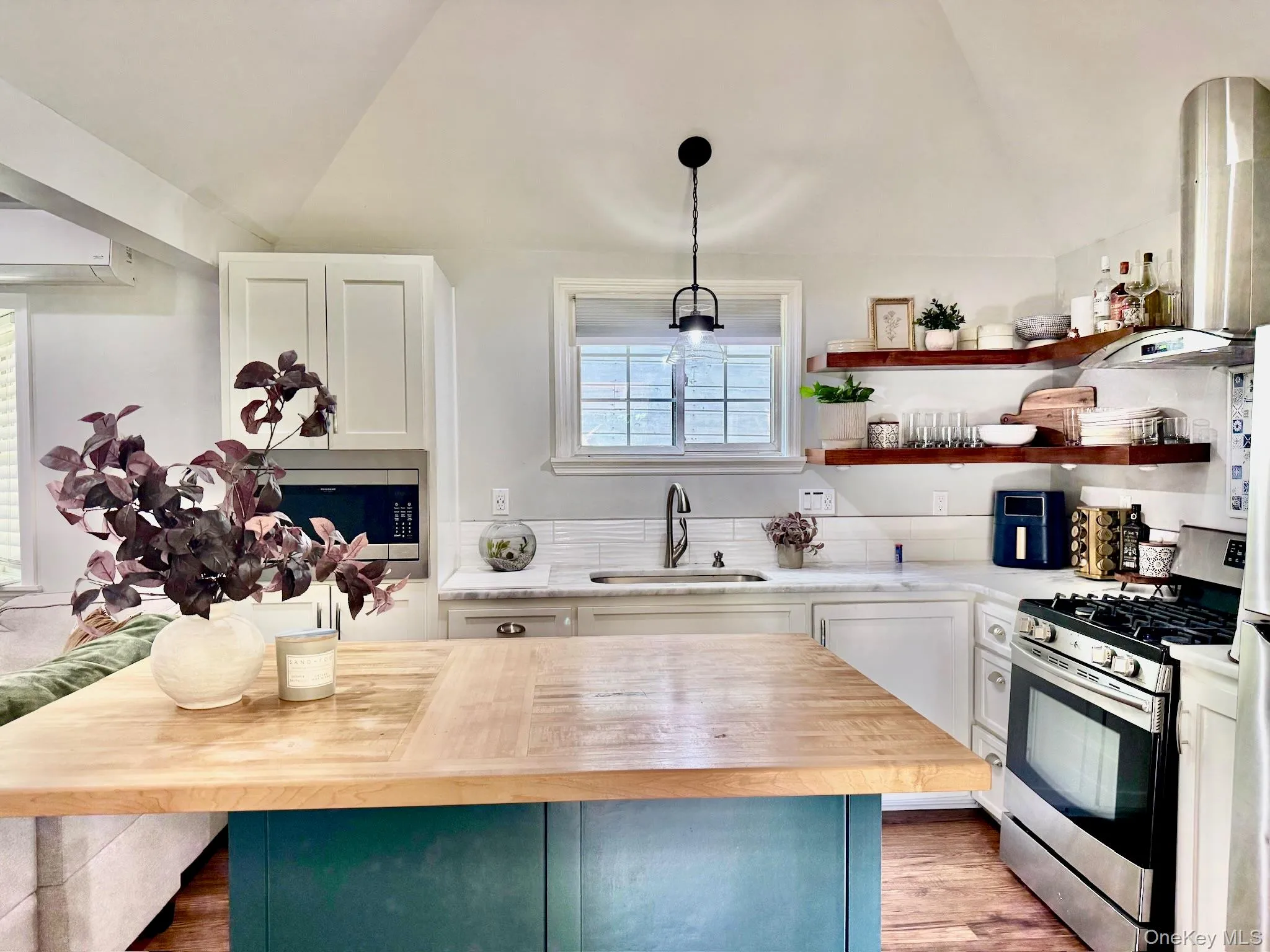 Cottage kitchen featuring a central island with a wood countertop, white shaker cabinetry, stainless steel appliances, and open wood shelving Cottage kitchen featuring a central island with a wood countertop, white shaker cabinetry, stainless steel appliances, and open wood shelving