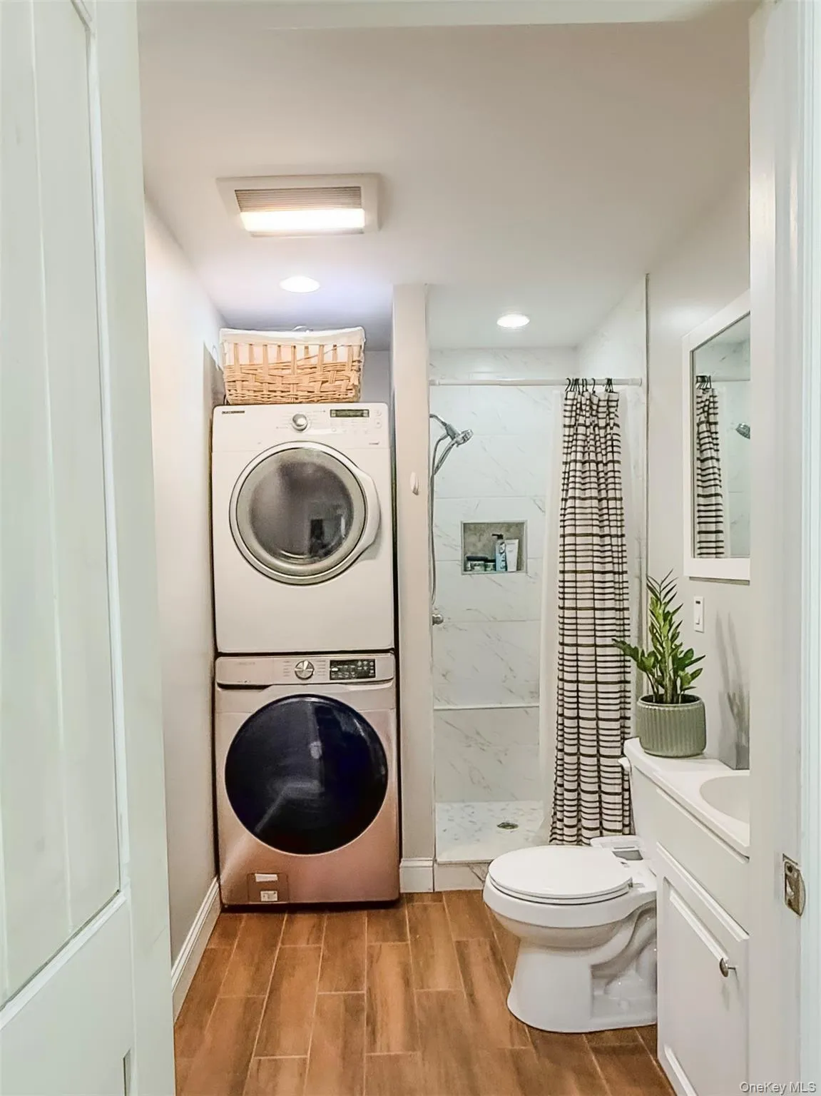 Cottage full bathroom with wood-finish flooring, stacked laundry appliances, walk-in shower with glass enclosure, recessed lighting, and a vanity with an integrated sink Cottage full bathroom with wood-finish flooring, stacked laundry appliances, walk-in shower with glass enclosure, recessed lighting, and a vanity with an integrated sink