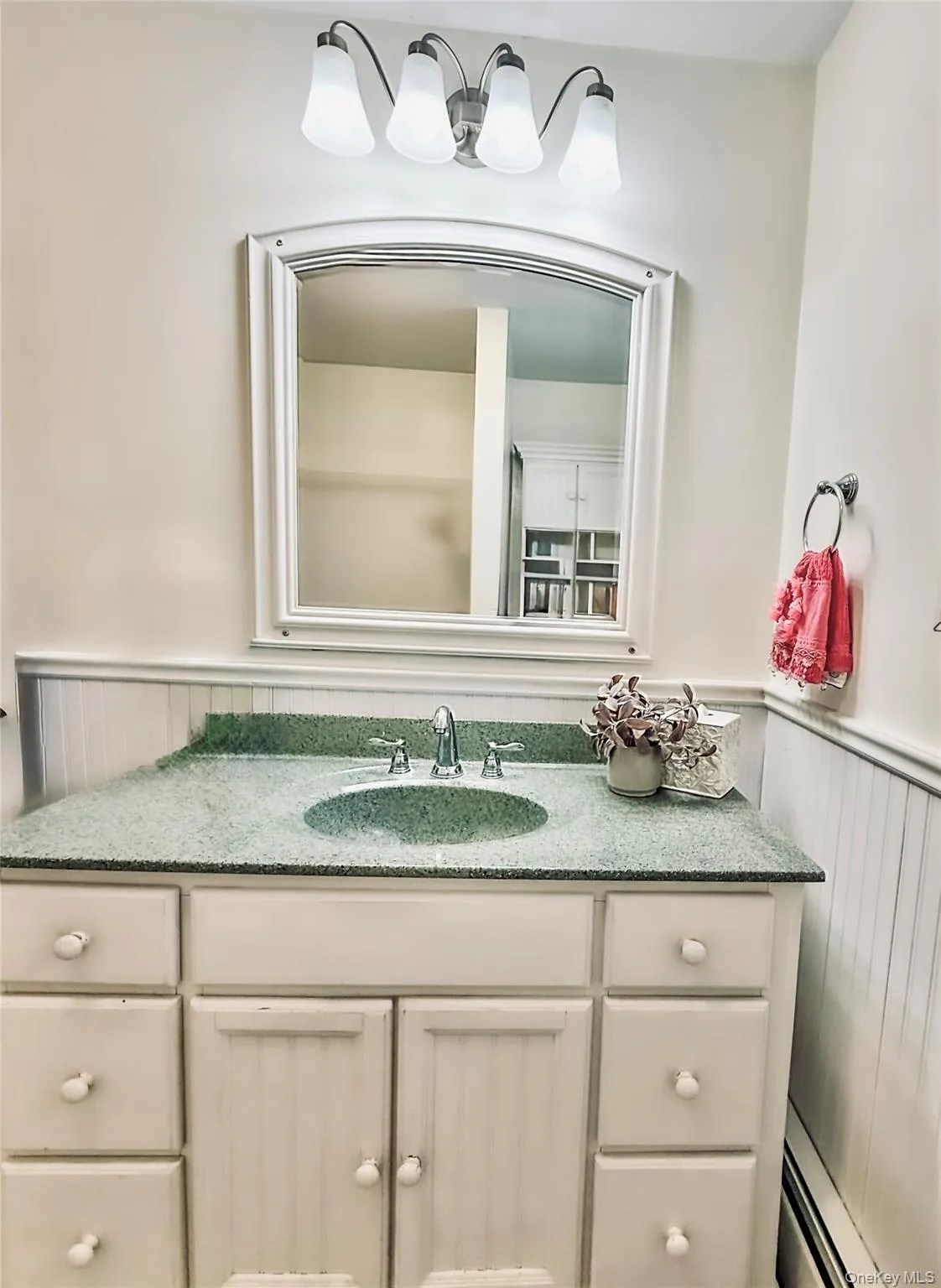 Lower apt bathroom vanity with a green speckled countertop and integrated sink, beadboard wainscoting, and a wall-mounted light fixture Lower apt bathroom vanity with a green speckled countertop and integrated sink, beadboard wainscoting, and a wall-mounted light fixture