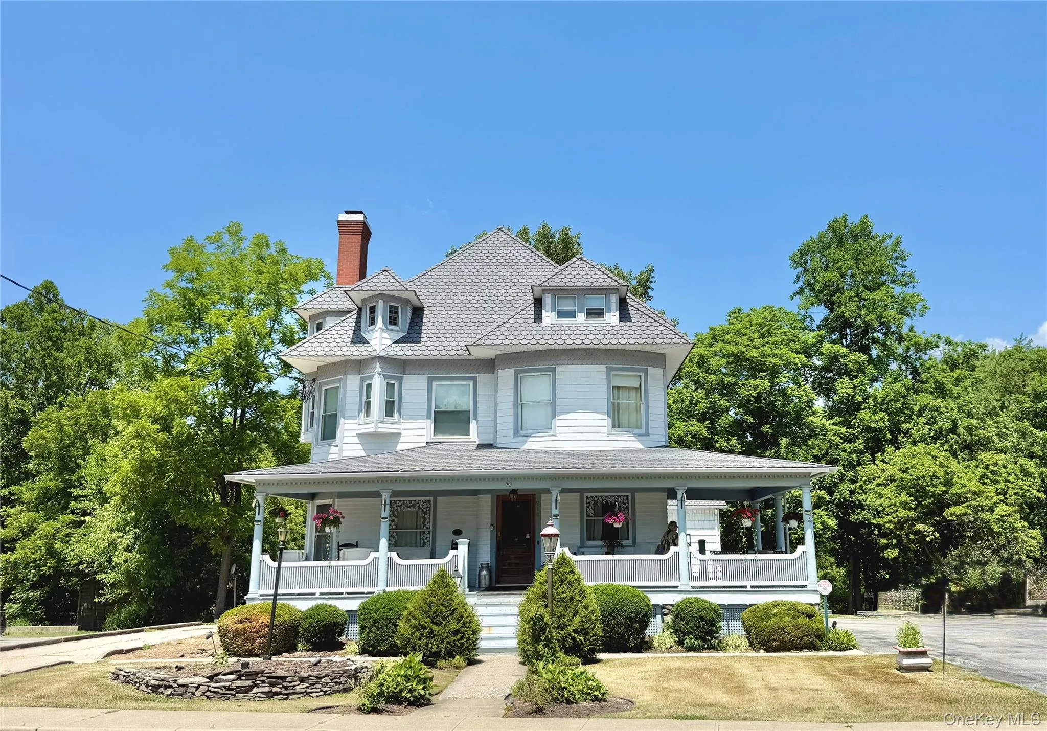 Victorian architecture featuring a wide covered porch, a prominent brick chimney, a multi-gabled roof, decorative dormer windows, and a structured front yard Victorian architecture featuring a wide covered porch, a prominent brick chimney, a multi-gabled roof, decorative dormer windows, and a structured front yard