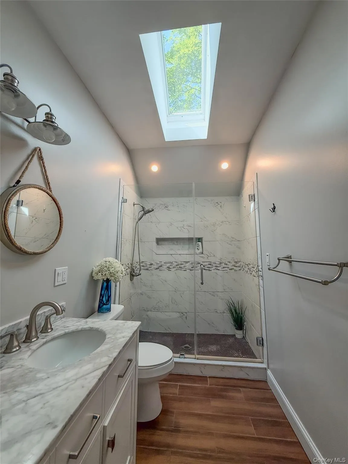 Cottage full bathroom with double vanity w/skylight feature, walk-in shower with glass enclosure and wood-finish flooring Cottage full bathroom with double vanity w/skylight feature, walk-in shower with glass enclosure and wood-finish flooring