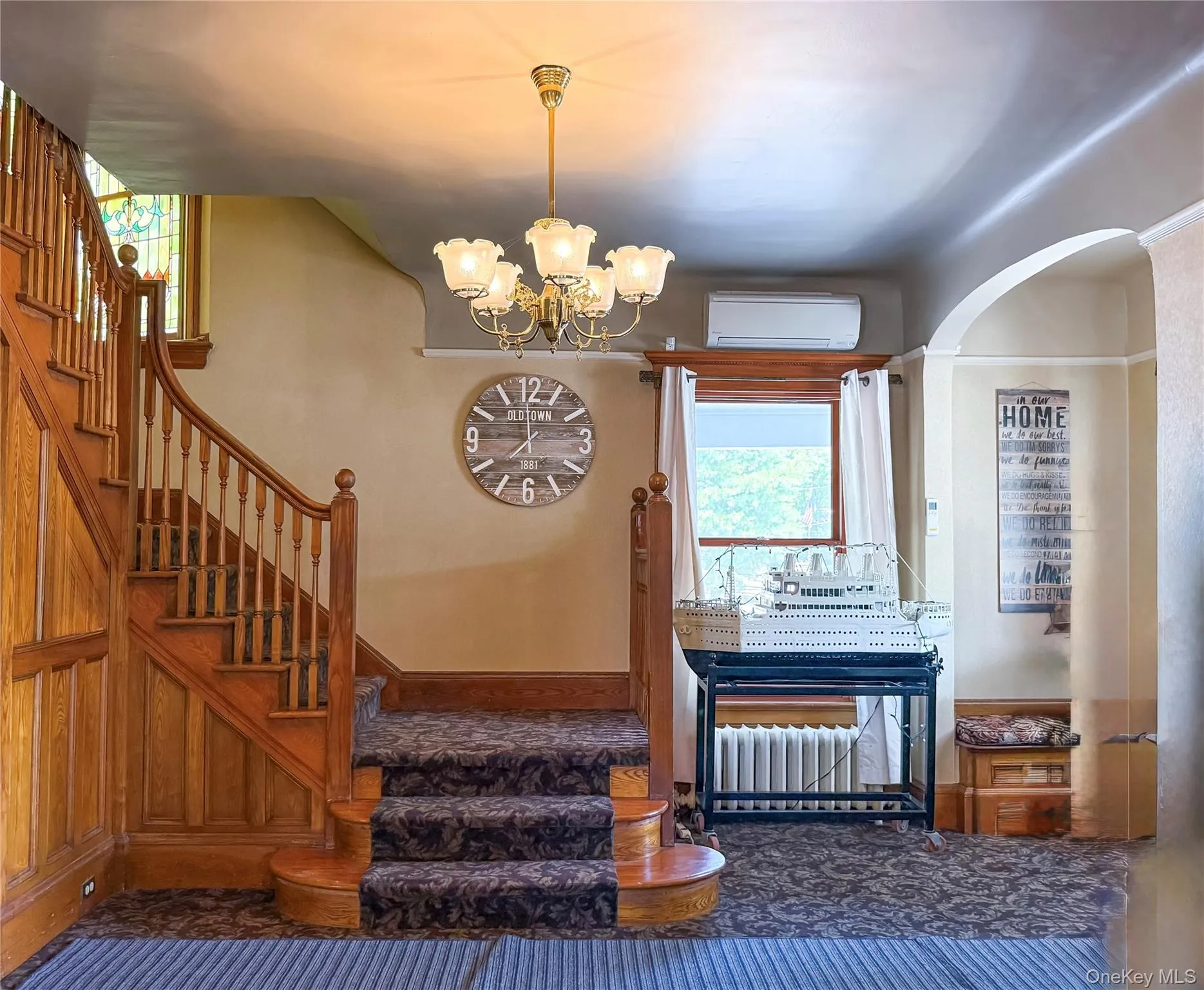 Grand Wood Staircase with carpeted and wood paneling, featuring a decorative chandelier and an arched doorway Grand Wood Staircase with carpeted and wood paneling, featuring a decorative chandelier and an arched doorway