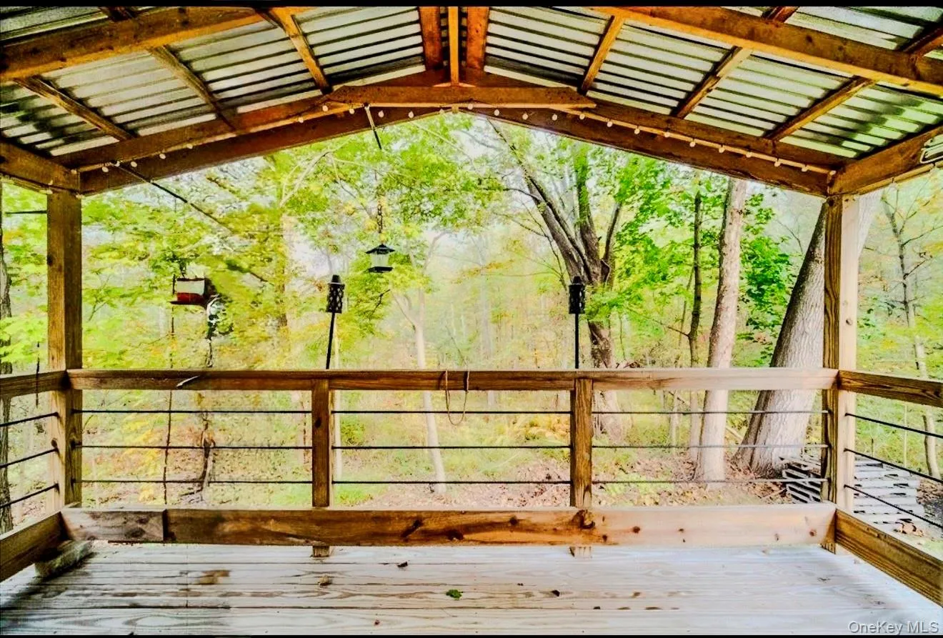 Cottage covered private deck with a corrugated metal roof, wood-finish flooring, and wood railings with black metal balusters Cottage covered private deck with a corrugated metal roof, wood-finish flooring, and wood railings with black metal balusters