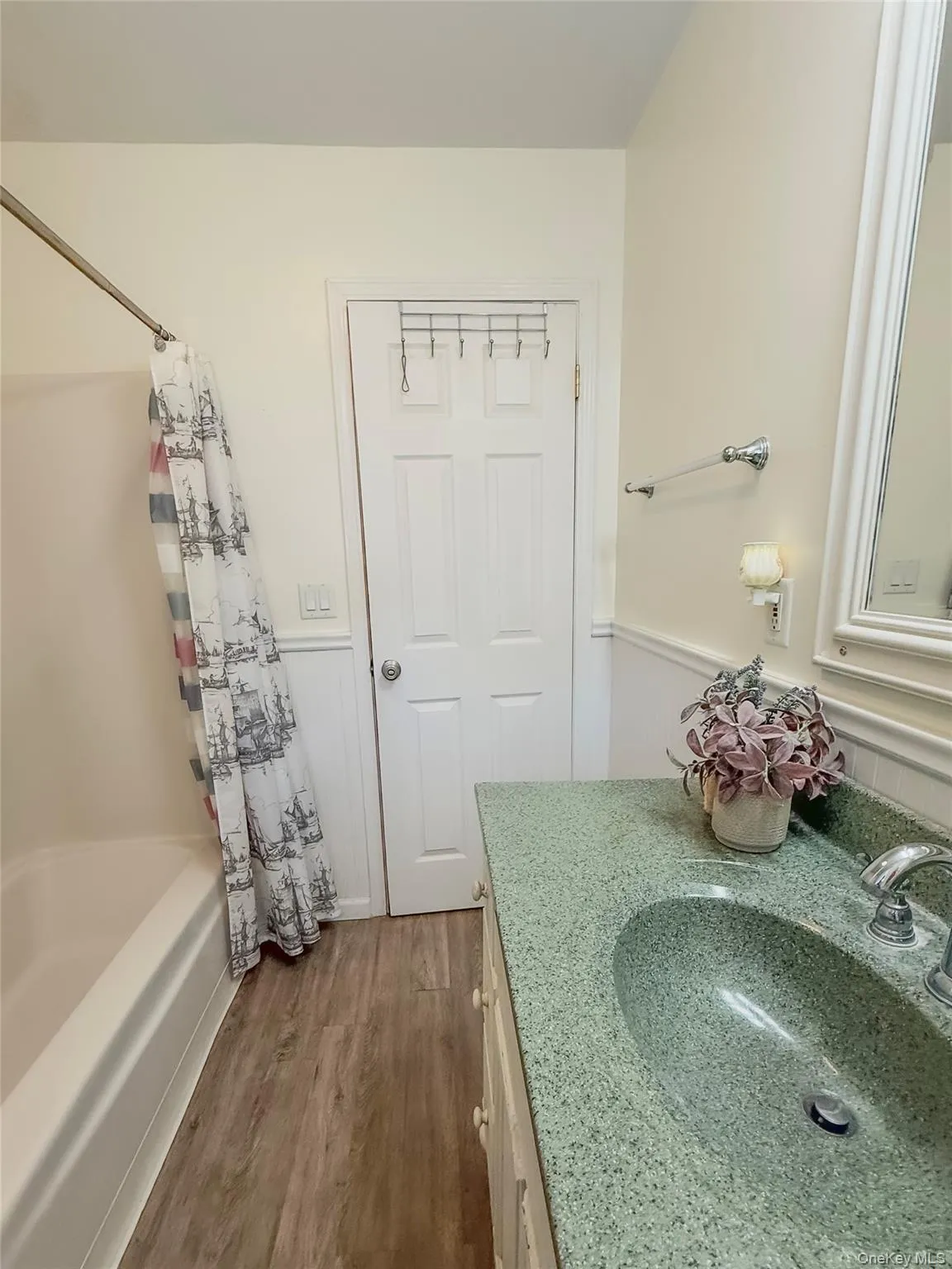 Lower apt bathroom vanity with a green speckled countertop and integrated sink, beadboard wainscoting, and a wall-mounted light fixture Lower apt bathroom vanity with a green speckled countertop and integrated sink, beadboard wainscoting, and a wall-mounted light fixture