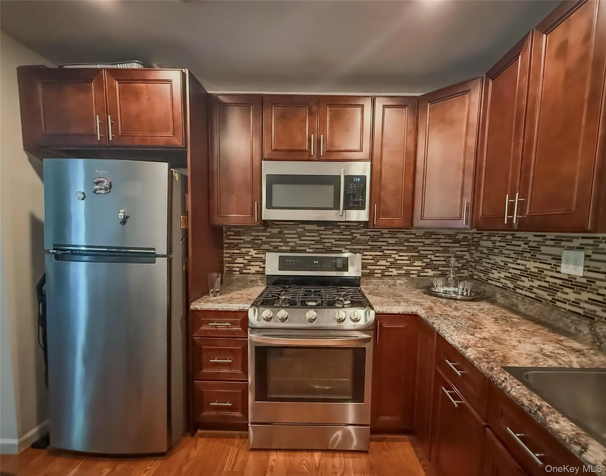Lower Apartment Kitchen featuring wood-finish cabinetry, stainless steel appliances, patterned backsplash, and an undermount sink Lower Apartment Kitchen featuring wood-finish cabinetry, stainless steel appliances, patterned backsplash, and an undermount sink