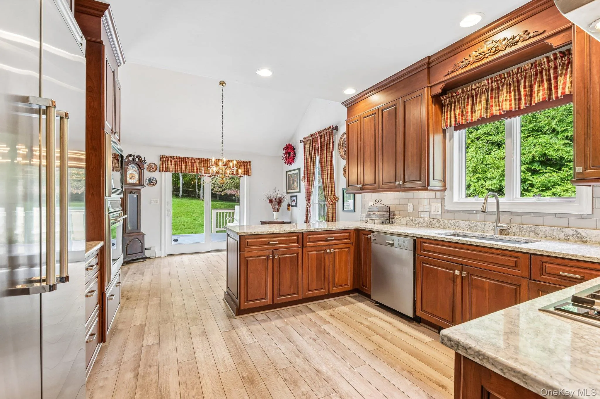 Spacious kitchen featuring wood-finish flooring, wood cabinetry, light-toned countertops, stainless steel appliances, and a vaulted ceiling Spacious kitchen featuring wood-finish flooring, wood cabinetry, light-toned countertops, stainless steel appliances, and a vaulted ceiling