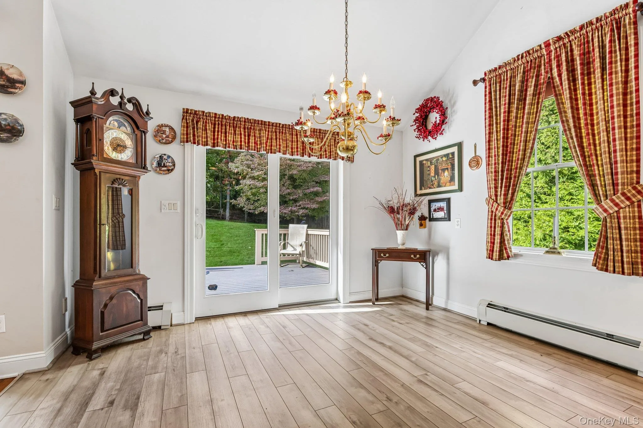 Light wood-finish flooring with a multi-pane window, brass chandelier, and a sliding glass door opening to an outdoor deck Light wood-finish flooring with a multi-pane window, brass chandelier, and a sliding glass door opening to an outdoor deck