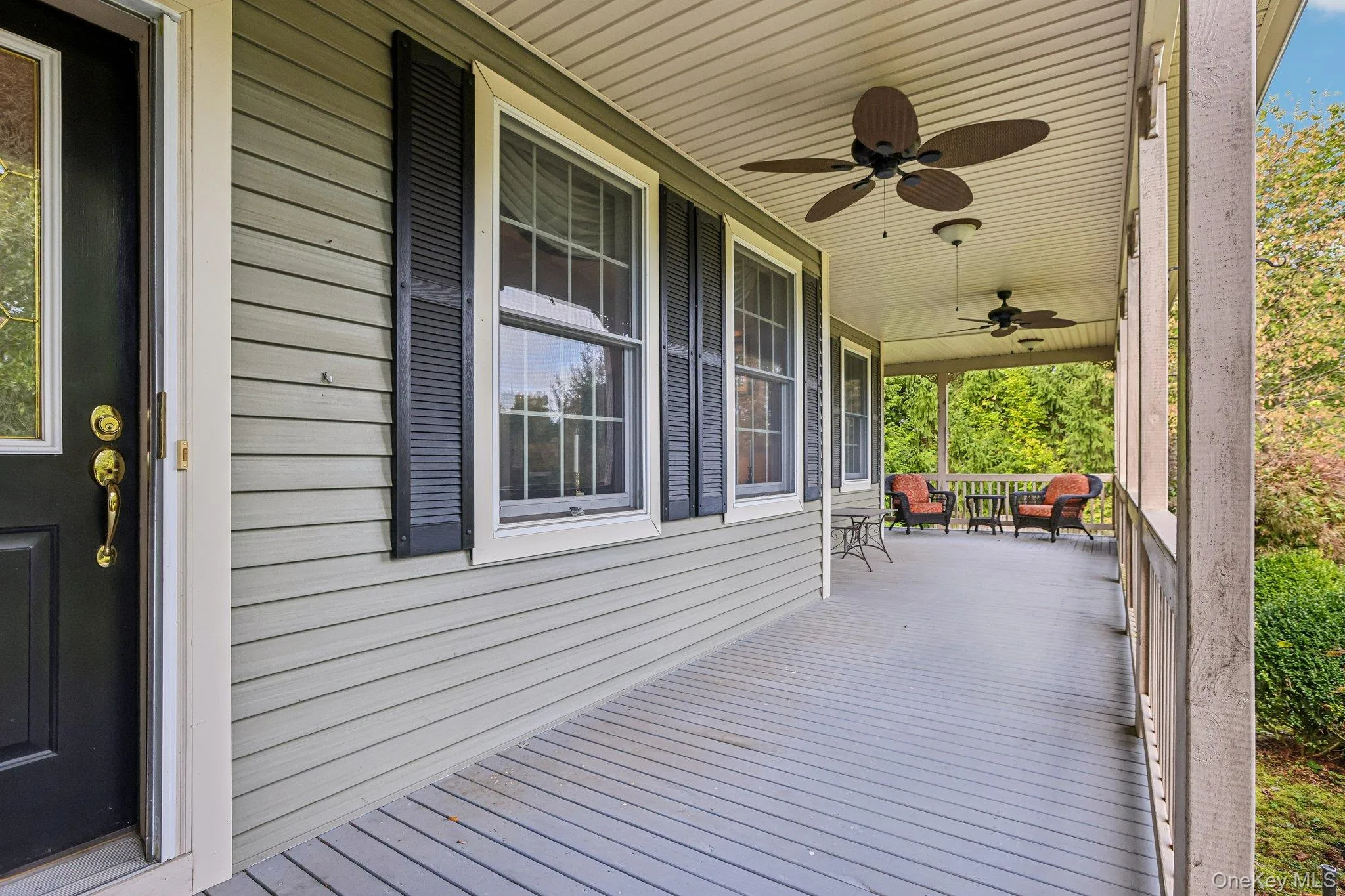 Expansive covered porch featuring ceiling fans, light-toned siding, and dark window shutters Expansive covered porch featuring ceiling fans, light-toned siding, and dark window shutters