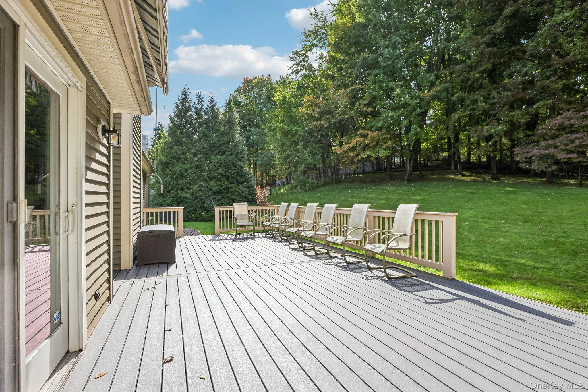 Expansive outdoor deck with railing, sliding glass door access, and a large manicured lawn surrounded by mature trees Expansive outdoor deck with railing, sliding glass door access, and a large manicured lawn surrounded by mature trees
