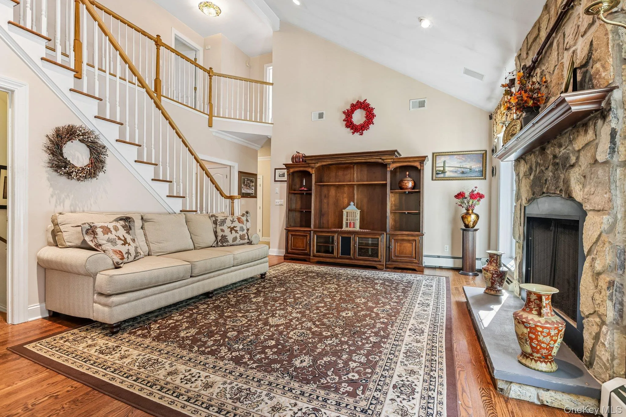 Stone fireplace with hearth, vaulted ceiling, wood-finish flooring, and a multi-level staircase with wood railings Stone fireplace with hearth, vaulted ceiling, wood-finish flooring, and a multi-level staircase with wood railings