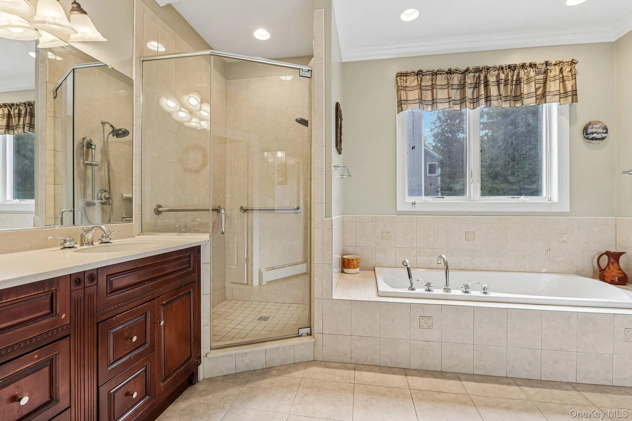 Built-in jetted tub with tile surround, corner glass-enclosed shower with tile, dark wood-finish vanity with countertop, undermount sink, and recessed lighting Built-in jetted tub with tile surround, corner glass-enclosed shower with tile, dark wood-finish vanity with countertop, undermount sink, and recessed lighting