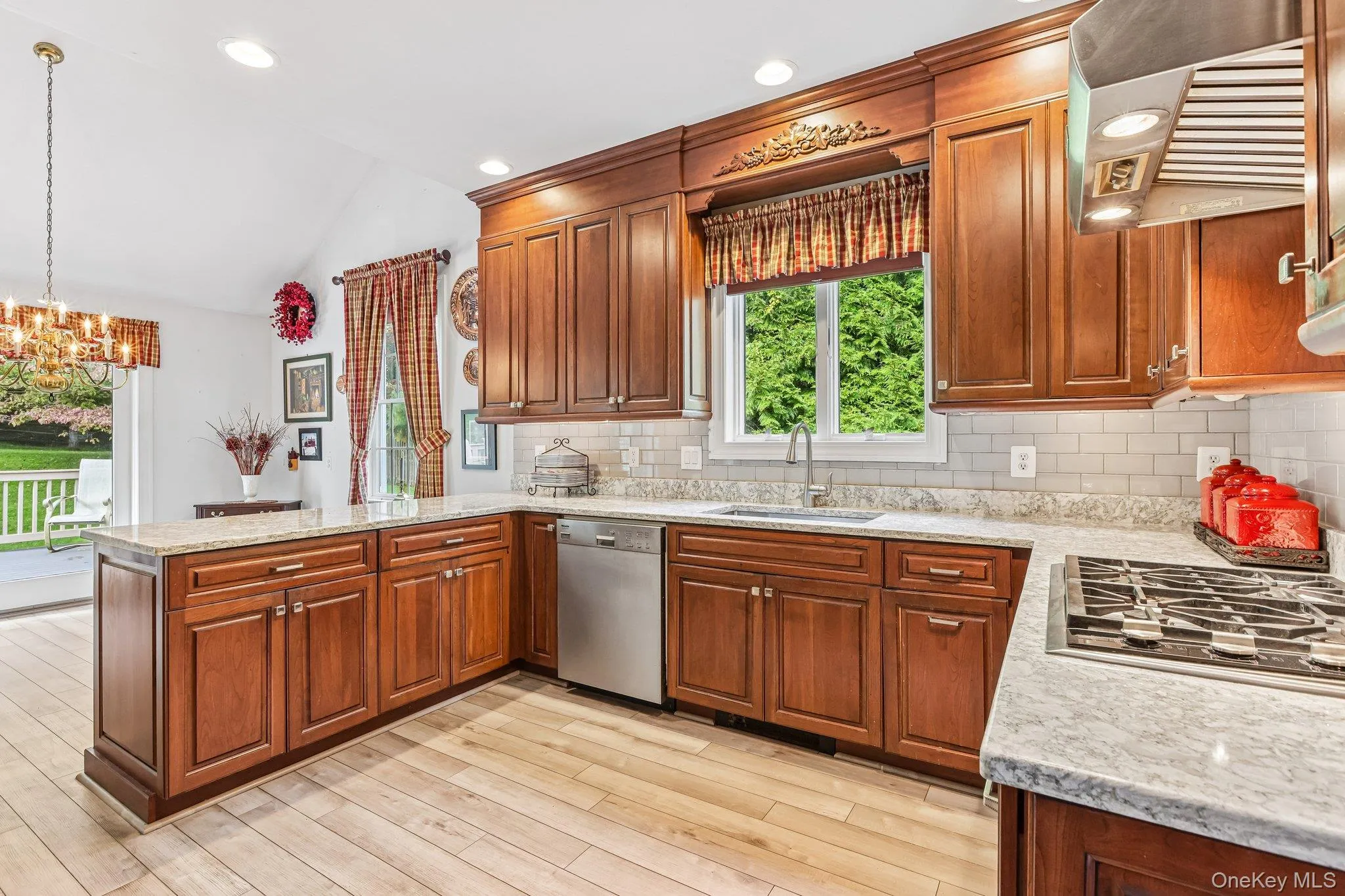 Kitchen featuring wood-finish flooring, ample wood cabinetry, light-toned countertops, a subway tile backsplash, and stainless steel appliances Kitchen featuring wood-finish flooring, ample wood cabinetry, light-toned countertops, a subway tile backsplash, and stainless steel appliances
