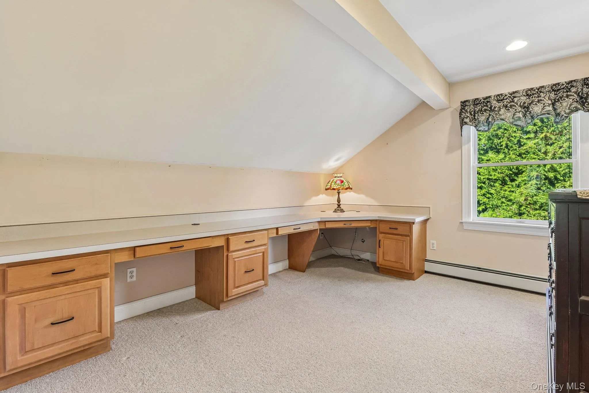 Built-in wood cabinetry with integrated desk space, sloped ceiling detail, and a window with exterior greenery Built-in wood cabinetry with integrated desk space, sloped ceiling detail, and a window with exterior greenery