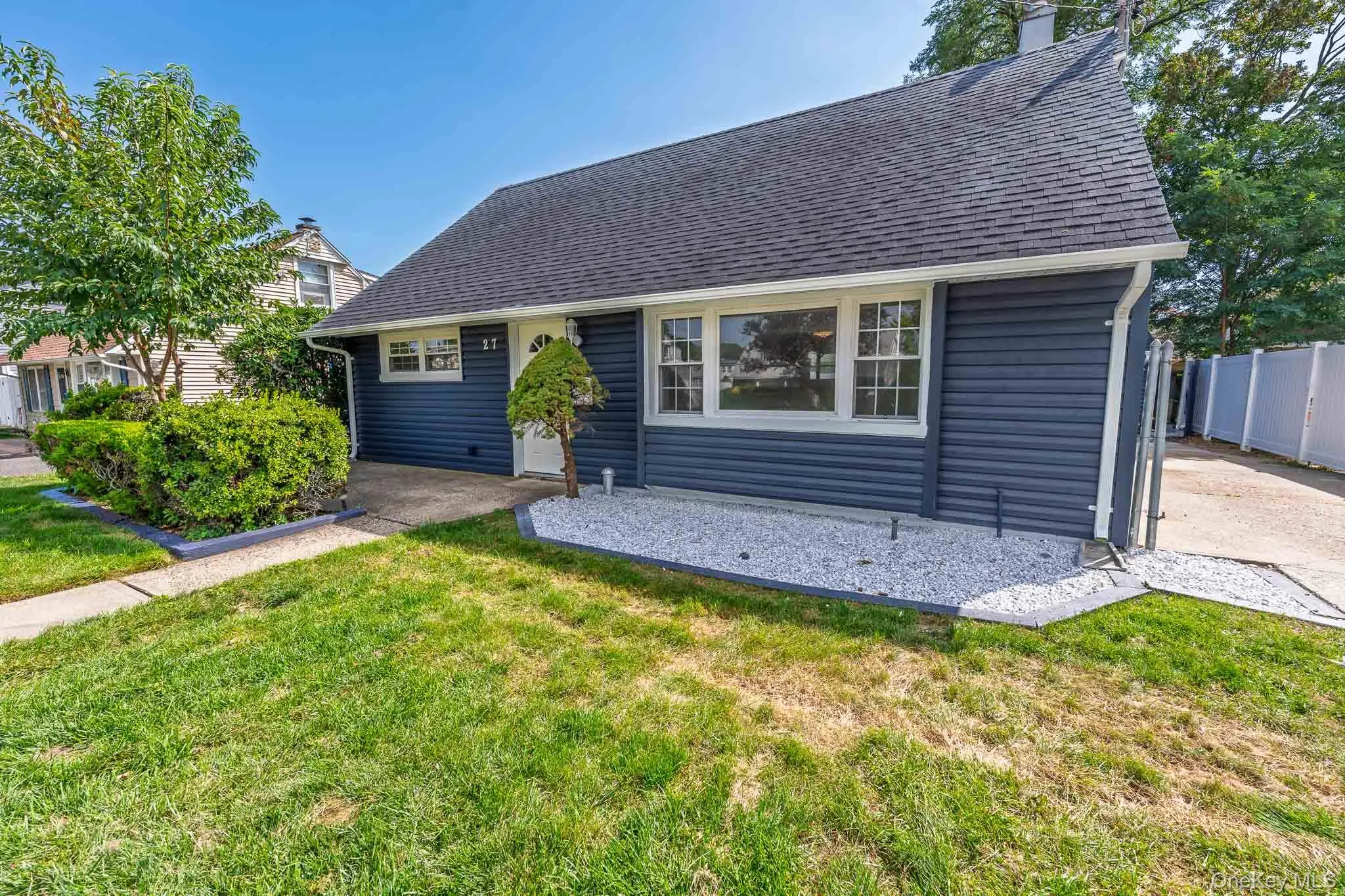Exterior featuring dark blue new siding, a dark shingle roof, white trim windows, a white front door, and a gravel bed Exterior featuring dark blue new siding, a dark shingle roof, white trim windows, a white front door, and a gravel bed