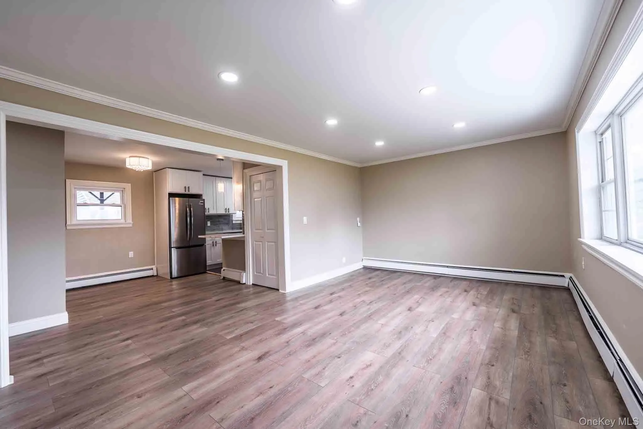 Recessed lighting, wood-finish vinyl flooring, white trim, stainless steel refrigerator, and white cabinetry Recessed lighting, wood-finish vinyl flooring, white trim, stainless steel refrigerator, and white cabinetry