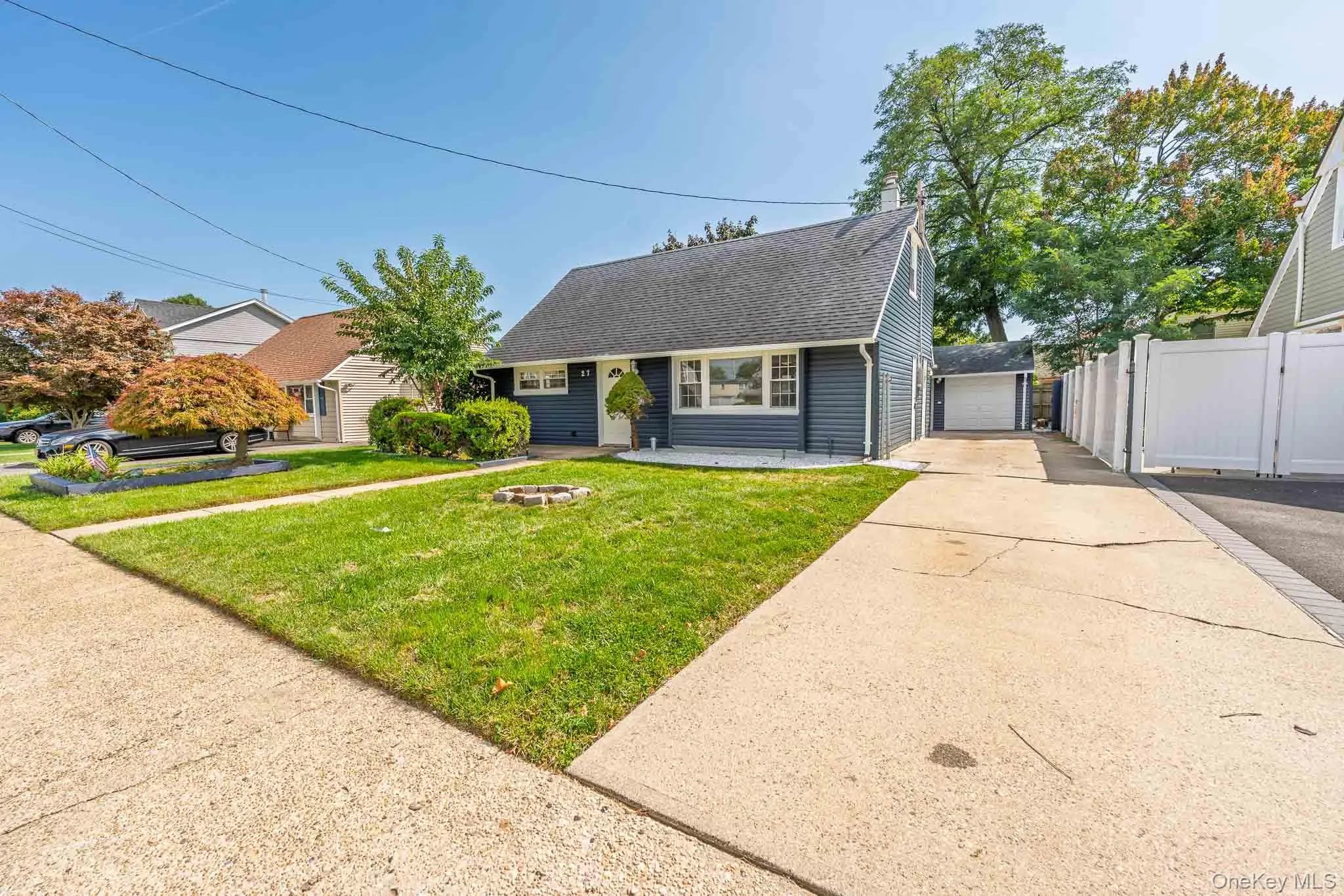 Blue siding exterior with a dark shingle roof, featuring a concrete driveway, a 2 car detached garage, and a white privacy fence Blue siding exterior with a dark shingle roof, featuring a concrete driveway, a 2 car detached garage, and a white privacy fence